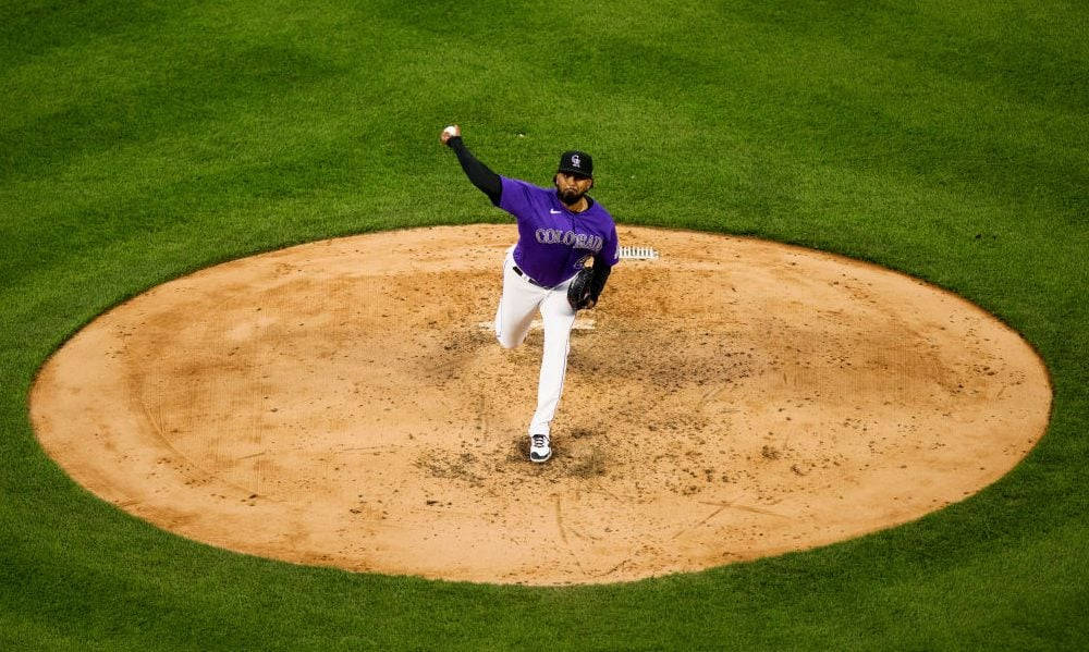 Pitch 桌布 壁紙 — 一名身穿紫色科羅拉多隊服的棒球投手，在充滿活力的綠色場地上從投手丘投球中。
