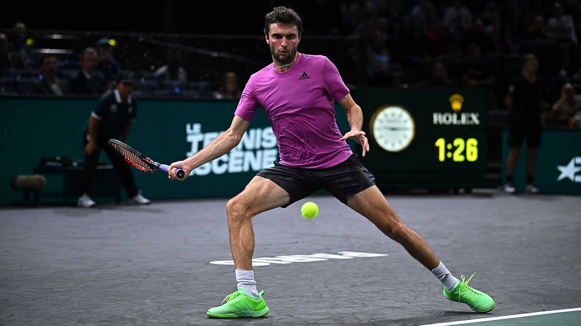 Athletic 桌布 壁紙 — 一名身穿紫色襯衫和螢光綠色鞋子的男網球運動員在明亮燈光下的硬地球場上飛身擊打黃色球。
