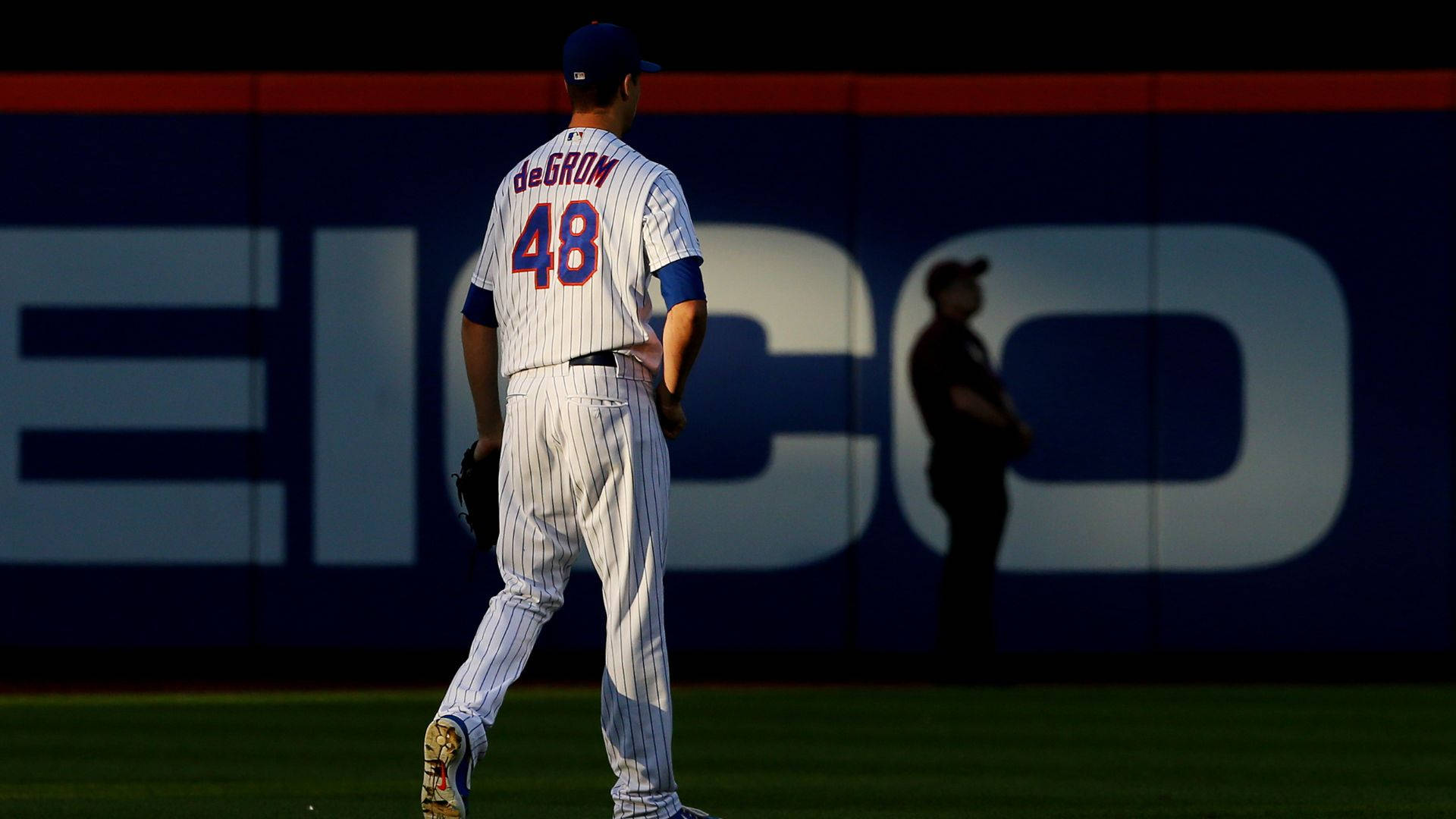 Degrom 桌布 壁紙 — 一名身穿細條紋球衣的棒球運動員在黃昏的球場上背對鏡頭走開，身後有一個巨大的「EICO」標誌。
