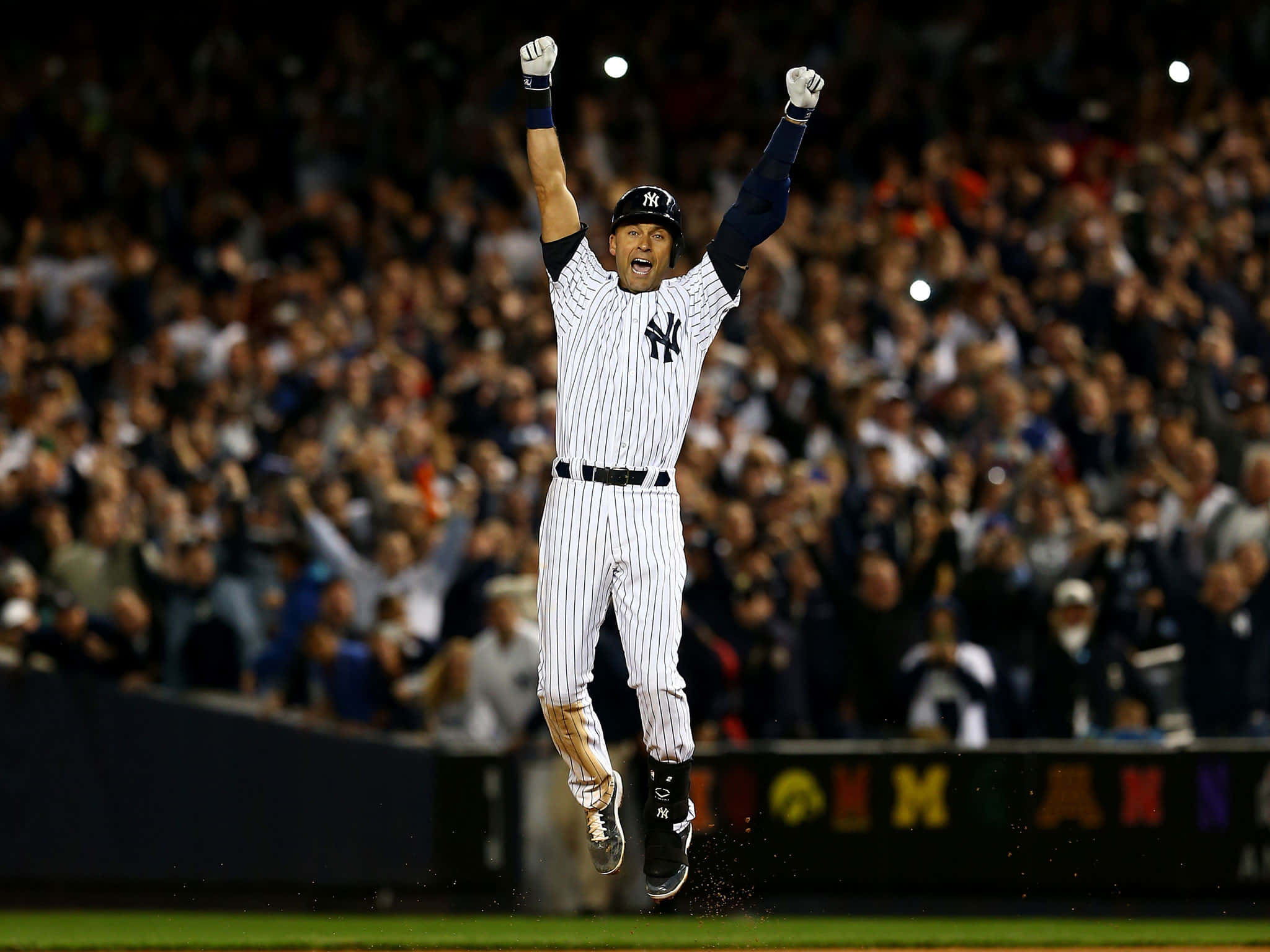 Derek Jeter 桌布 壁紙 — 一名身穿細條紋球衣的棒球選手，在燈光球場上高舉雙臂，歡欣跳躍，面前是歡呼的人群。