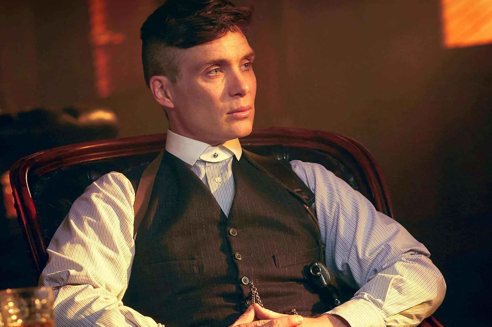 身穿細條紋背心的男士坐在皮革椅上，旁邊有威士忌杯。 — Peaky Blinders 壁紙