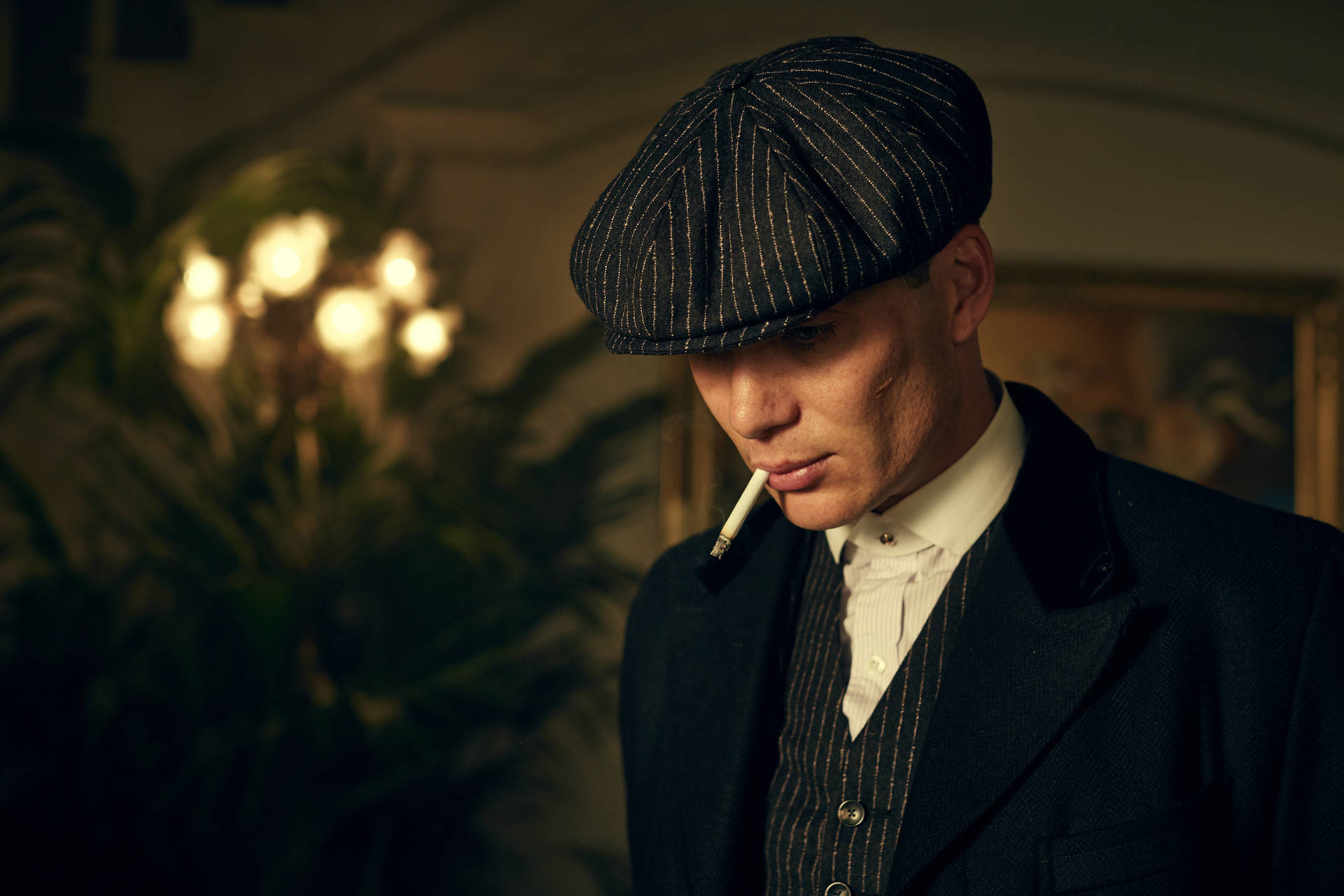 身穿復古西裝和帽子的男子在室內溫暖的吊燈光下抽煙。 — Peaky Blinders 壁紙