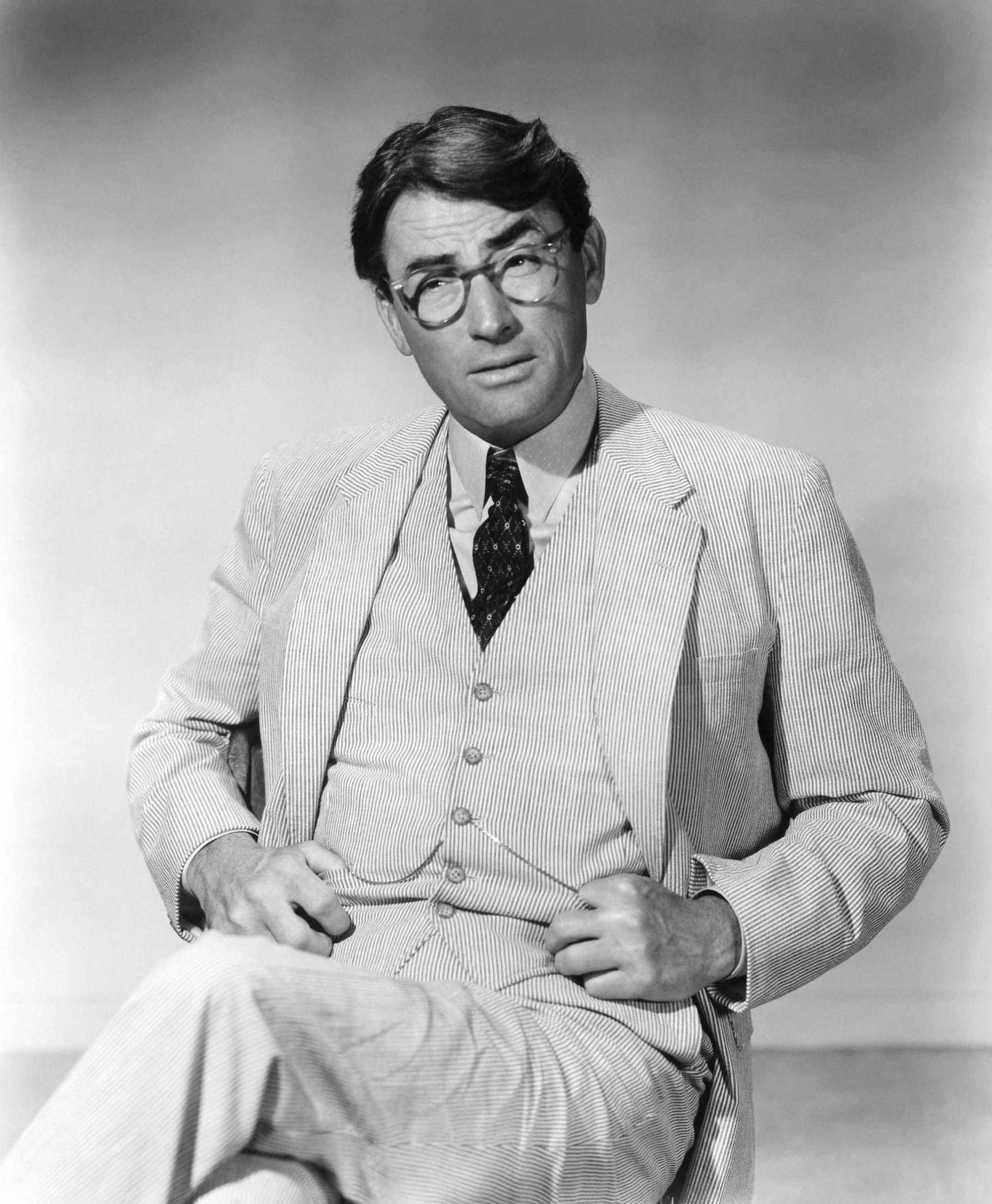 actor 桌布 壁紙 — 一名身穿細條紋西裝和眼鏡的男子，雙手放在翻領上，坐在純色攝影棚背景前。