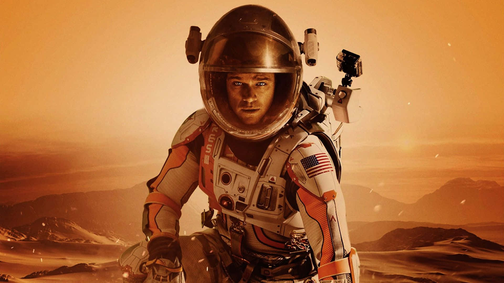 The Martian 桌布 壁紙 — 一名身穿細節豐富太空衣的太空人，站在佈滿灰塵的橙色火星景觀上，遠方有山脈，天空朦朧。