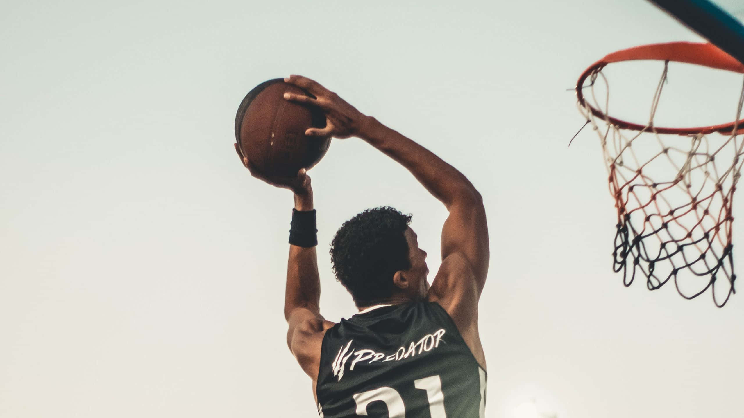 桌布 壁紙 — 一名身穿綠色 'PREDATOR' 球衣的籃球運動員，在淡色天空下以高度專注力灌籃。