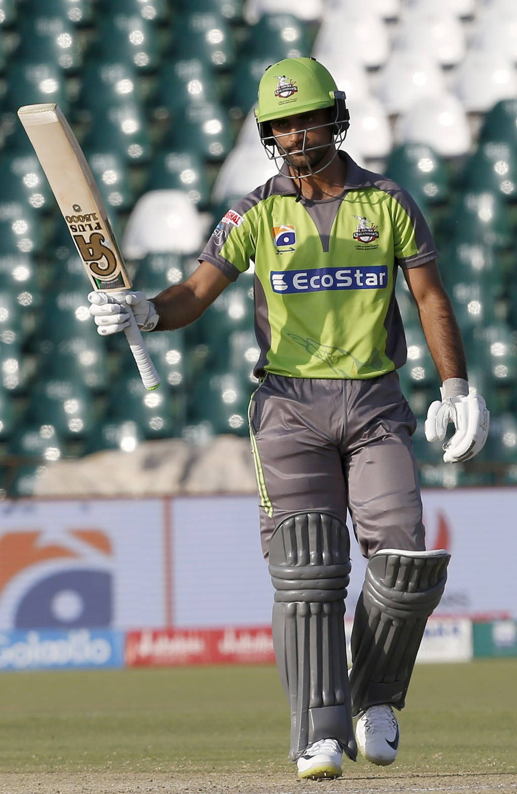 Fakhar Zaman 桌布 壁紙 — 一名身穿綠色和灰色裝備的板球運動員手持球棒離開球場，身後是模糊的空體育場座位。