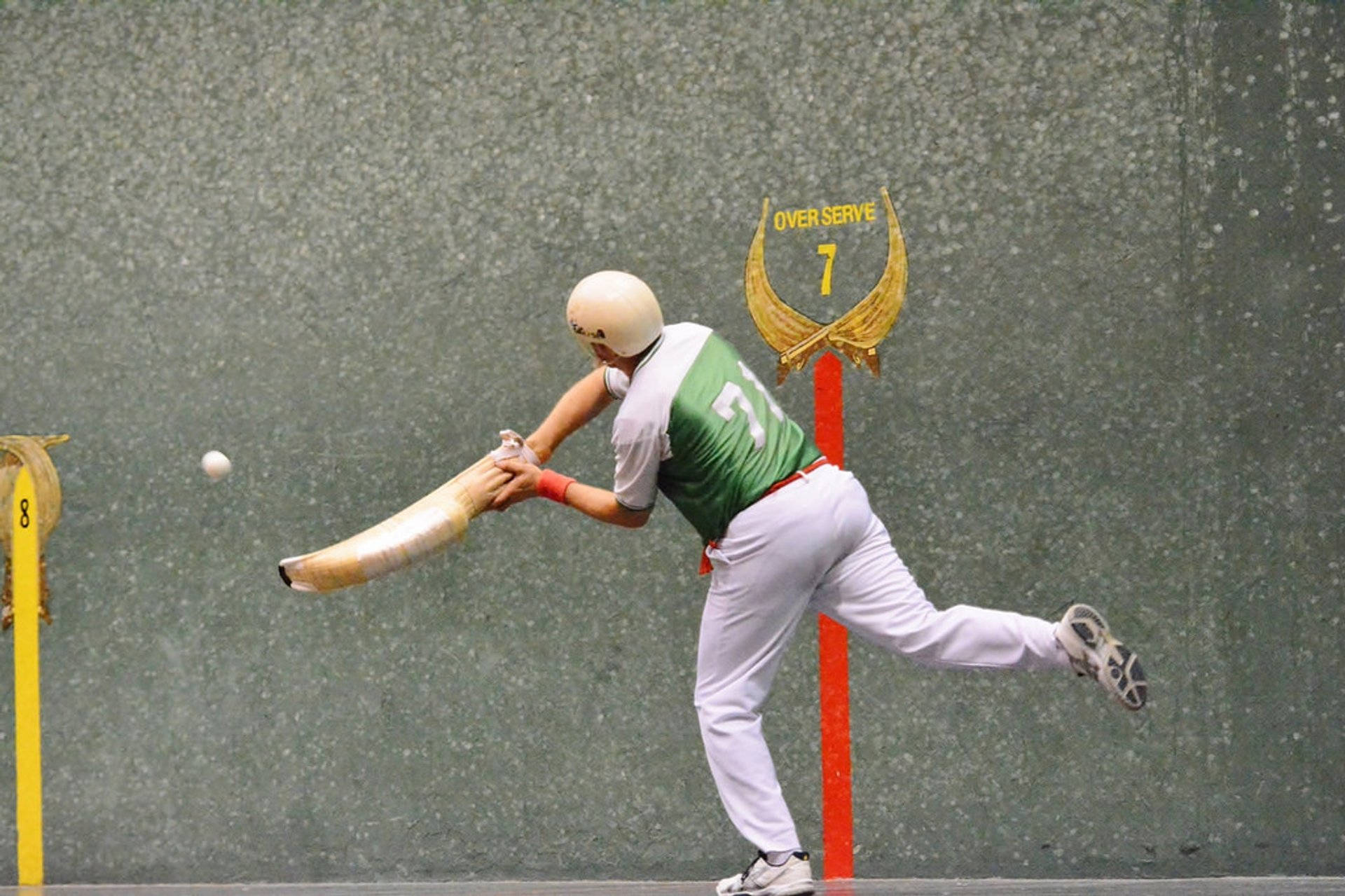 Athletic 桌布 壁紙 — 一名身穿綠色和白色球衣的球員，向著標有 'OVER SERVE 7' 的紋理牆壁揮動長球拍擊球。