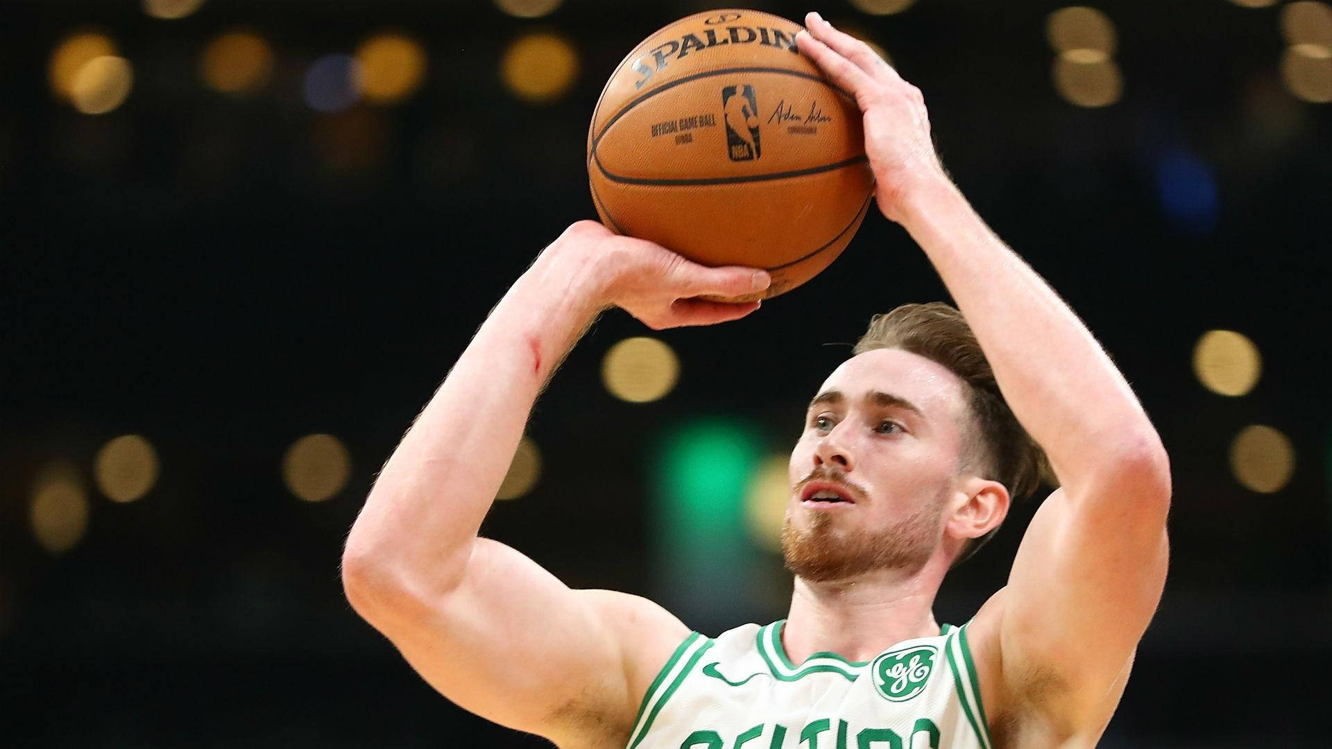 gordon hayward 桌布 壁紙 — 一名身穿綠色和白色球衣的籃球運動員在場館燈光下準備投擲Spalding NBA籃球。