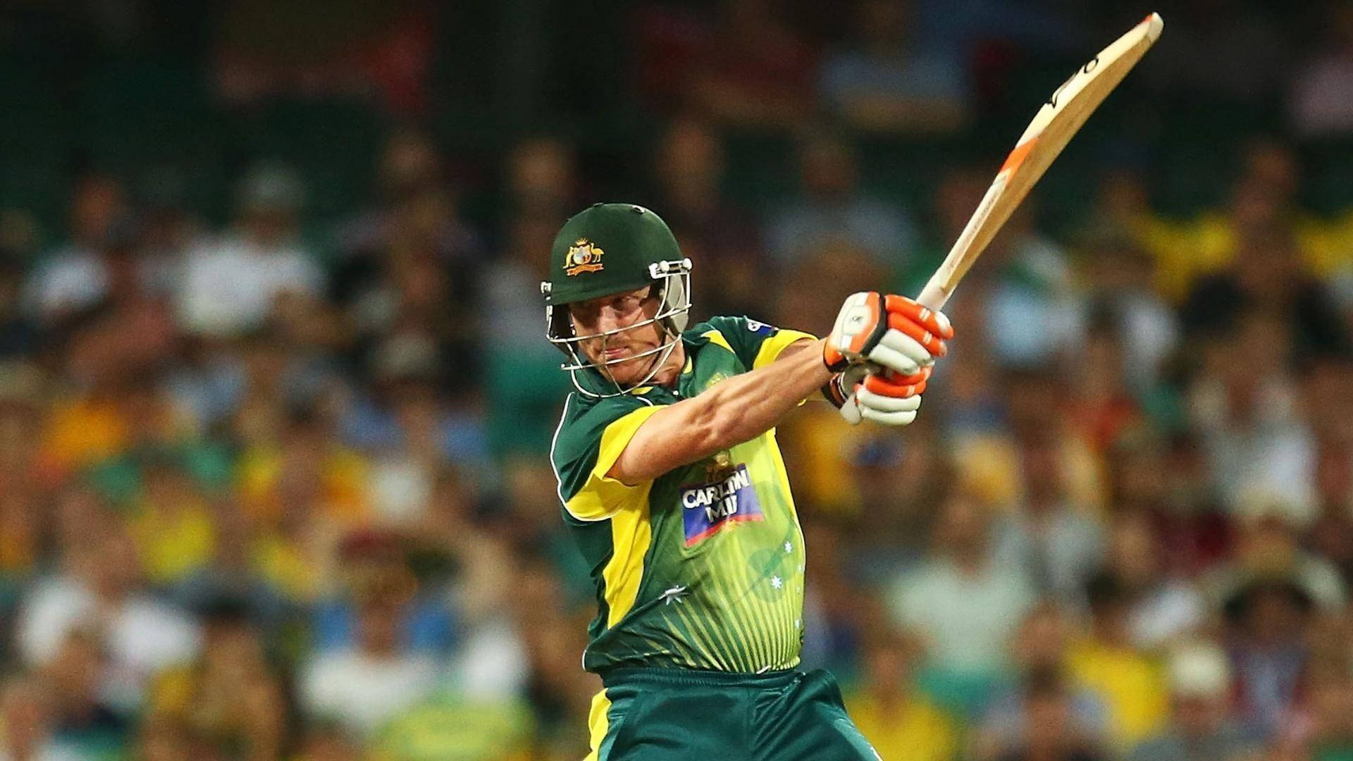 australia cricket 桌布 壁紙 — 一名身穿綠色和金色球衣的板球擊球手在體育場燈光下的夜間比賽中強力揮動球棒。