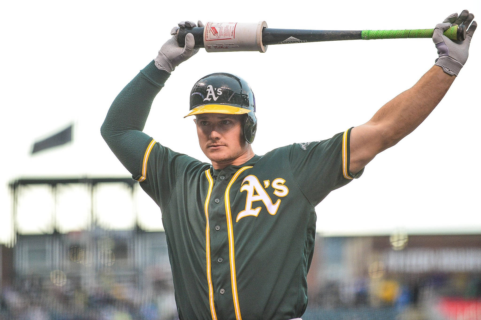 baseball bat 桌布 壁紙 — 一名身穿綠色和金色球衣的棒球選手，在明亮的球場背景下高舉球棒，擺出準備姿勢。
