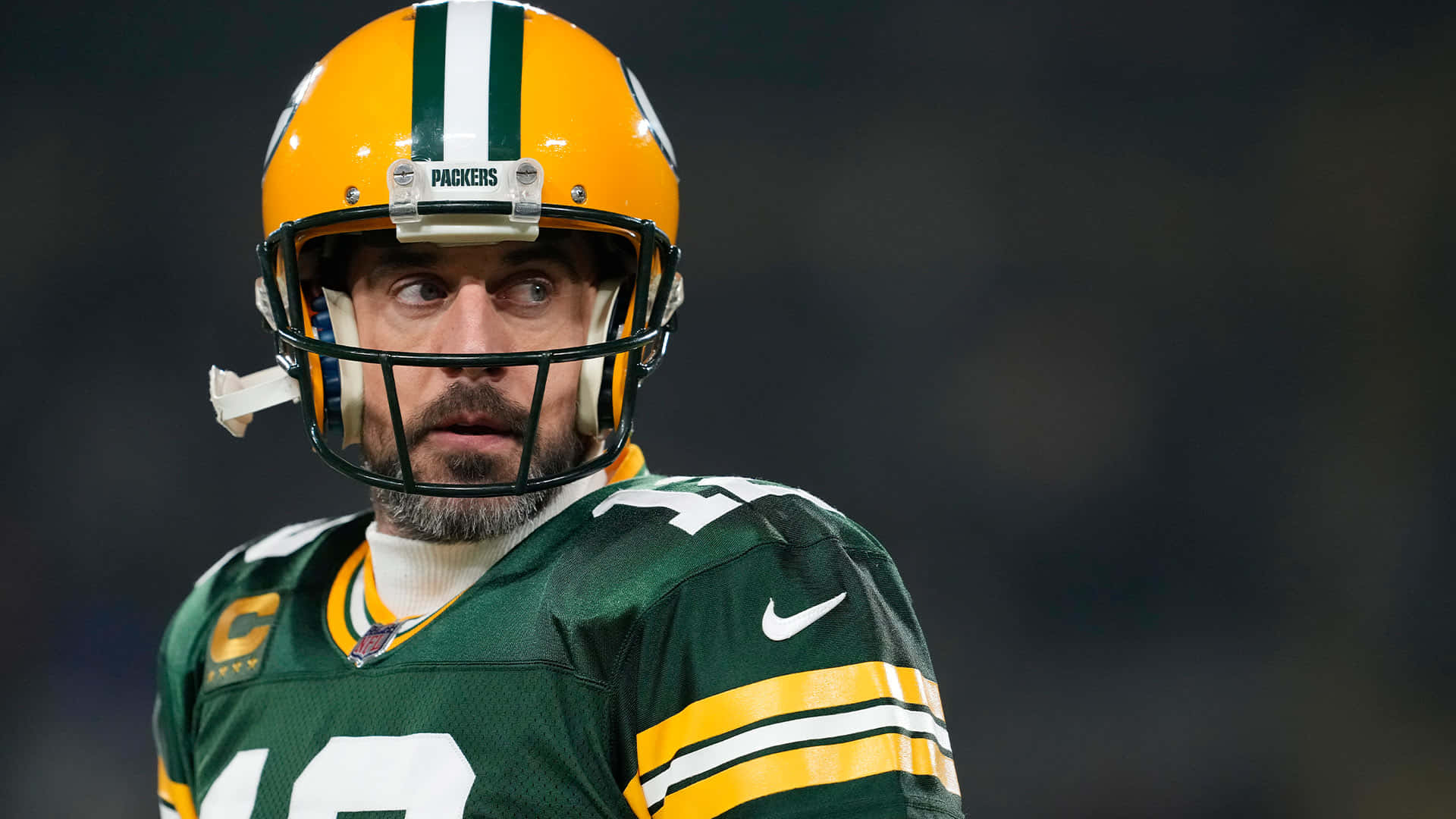 Aaron Rodgers 桌布 壁紙 — 一名身穿綠色和金色球衣的綠灣包裝工美式足球員在球場燈光下專注地望向鏡頭外。