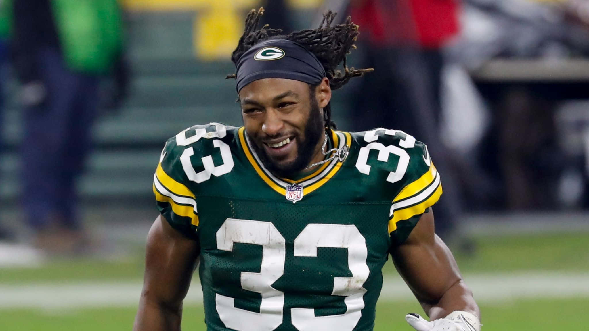 Aaron Jones 桌布 壁紙 — 一名身穿綠色和金色球衣的綠灣包裝工美式足球員在球場上奔跑時露出燦爛的笑容。