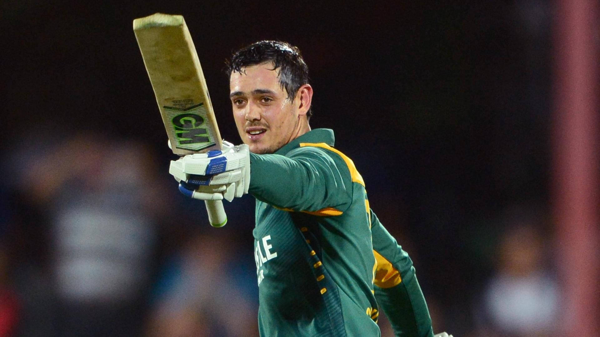 quinton de kock 桌布 壁紙 — 一名身穿綠色和黃色制服的板球運動員在體育場燈光下高舉球棒，表情勝利。