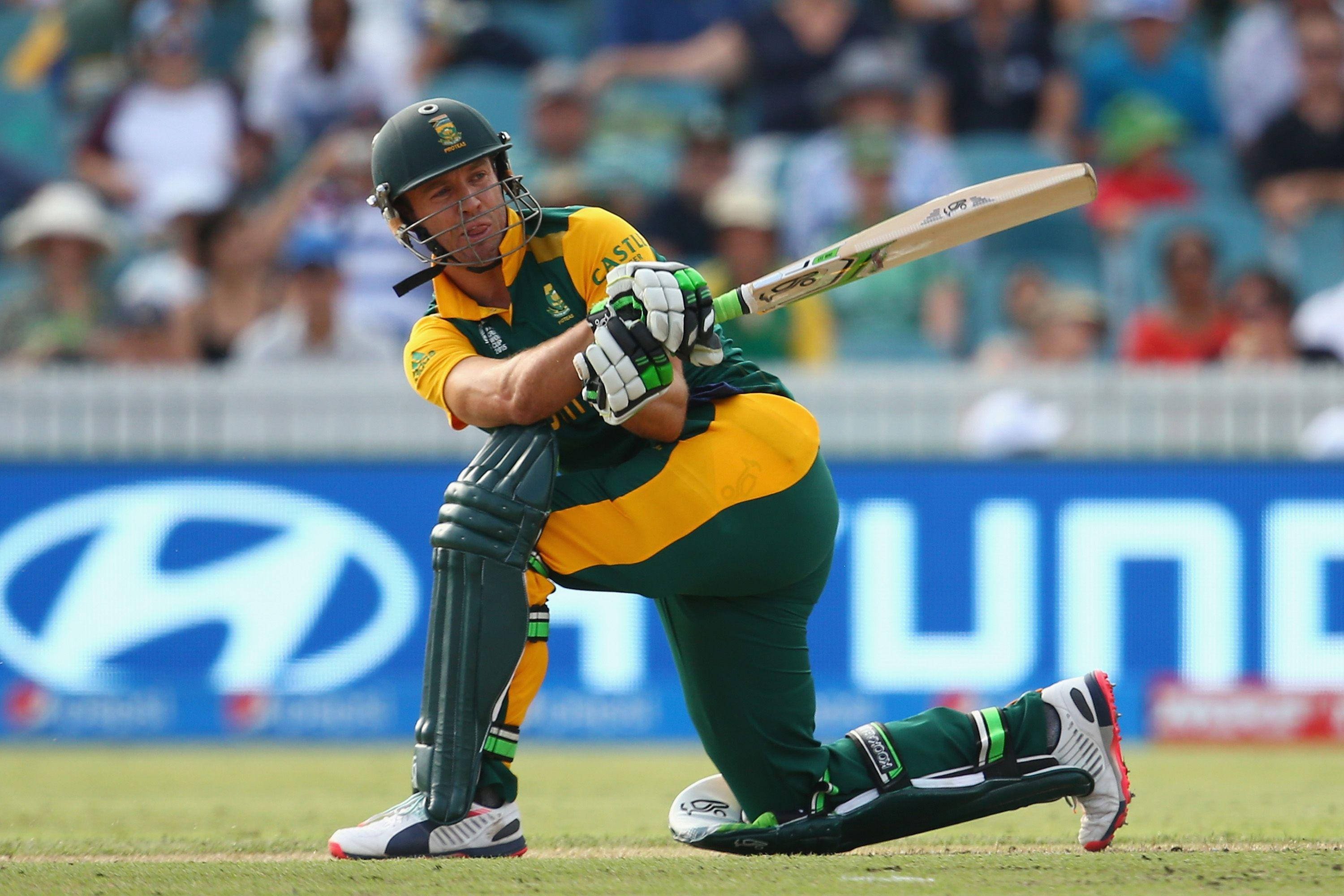 Ab De Villiers 桌布 壁紙 — 一名身穿綠色和黃色球衣的板球擊球手在陽光明媚的球場上揮動球棒，背景有模糊的觀眾。