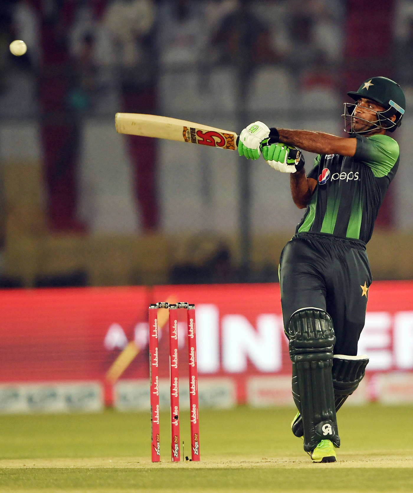 Fakhar Zaman 桌布 壁紙 — 一名身穿綠色和黑色制服的巴基斯坦板球擊球手在夜間比賽中，在體育場燈光下揮動球棒擊球。