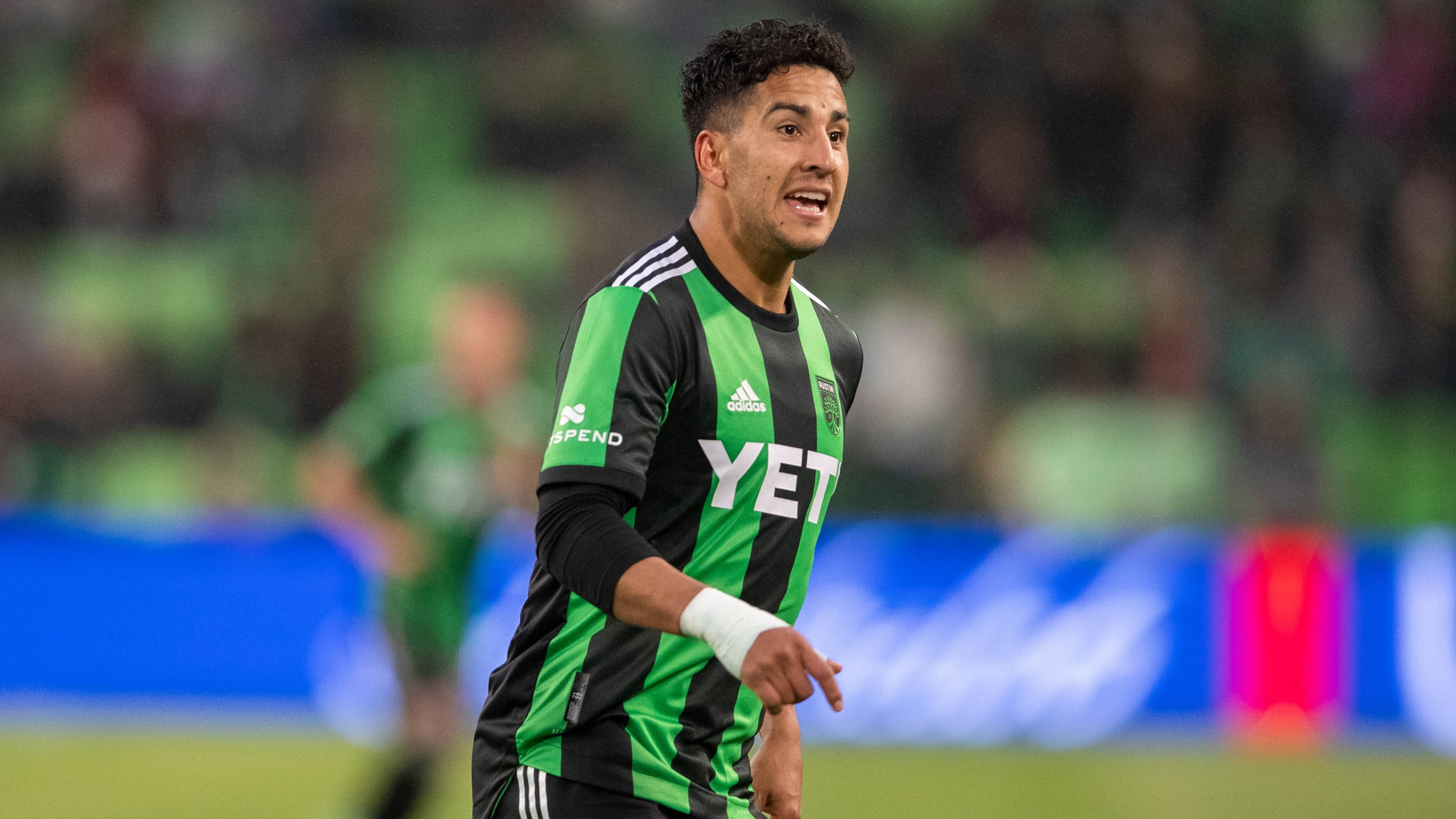 Austin Fc 桌布 壁紙 — 一名身穿綠色和黑色條紋球衣的足球運動員在燈光明亮的球場上以強烈的表情慶祝。