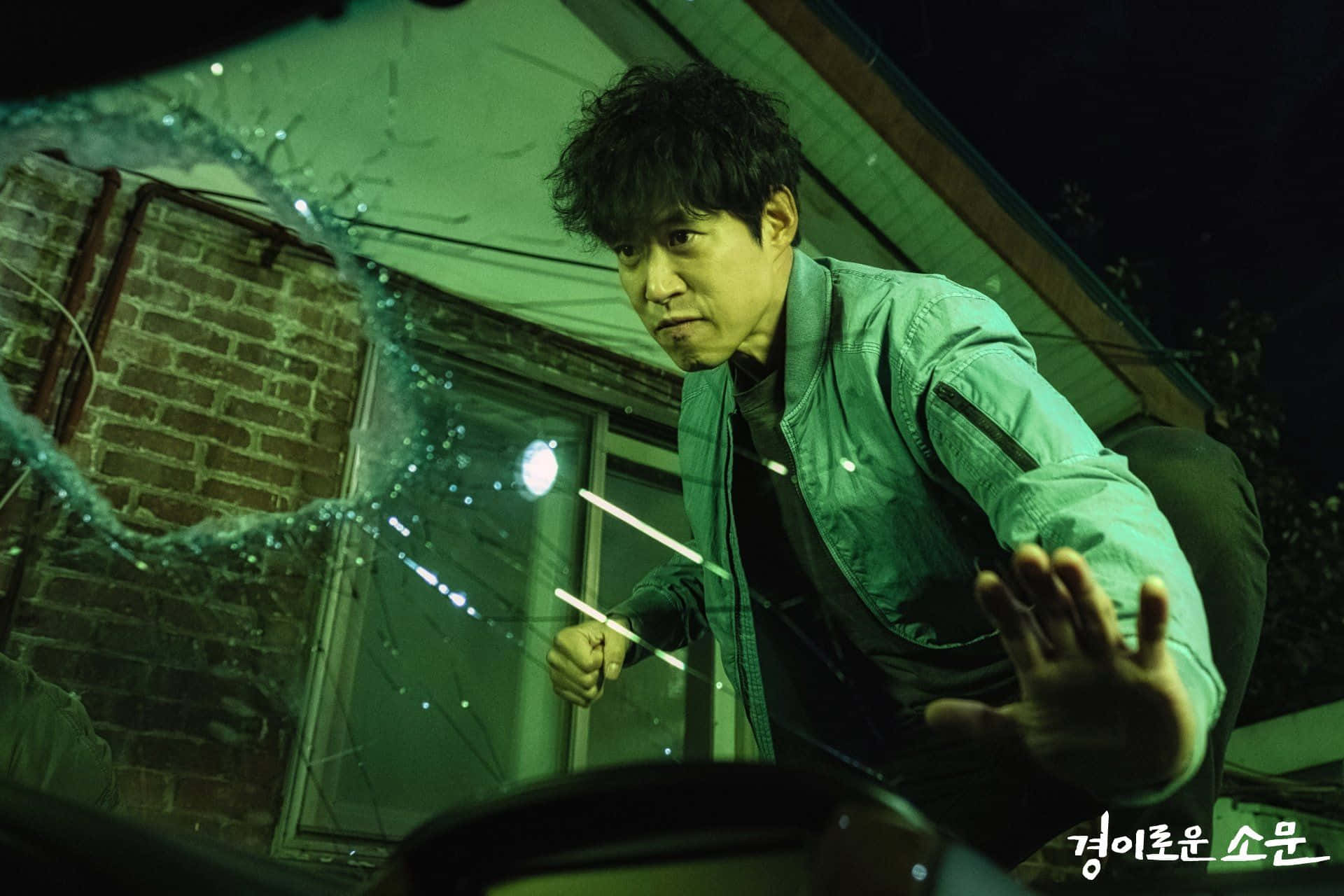 korean 桌布 壁紙 — 一名身穿綠色外套的男子在夜間帶著緊張的表情從破碎的汽車擋風玻璃中探出身子。