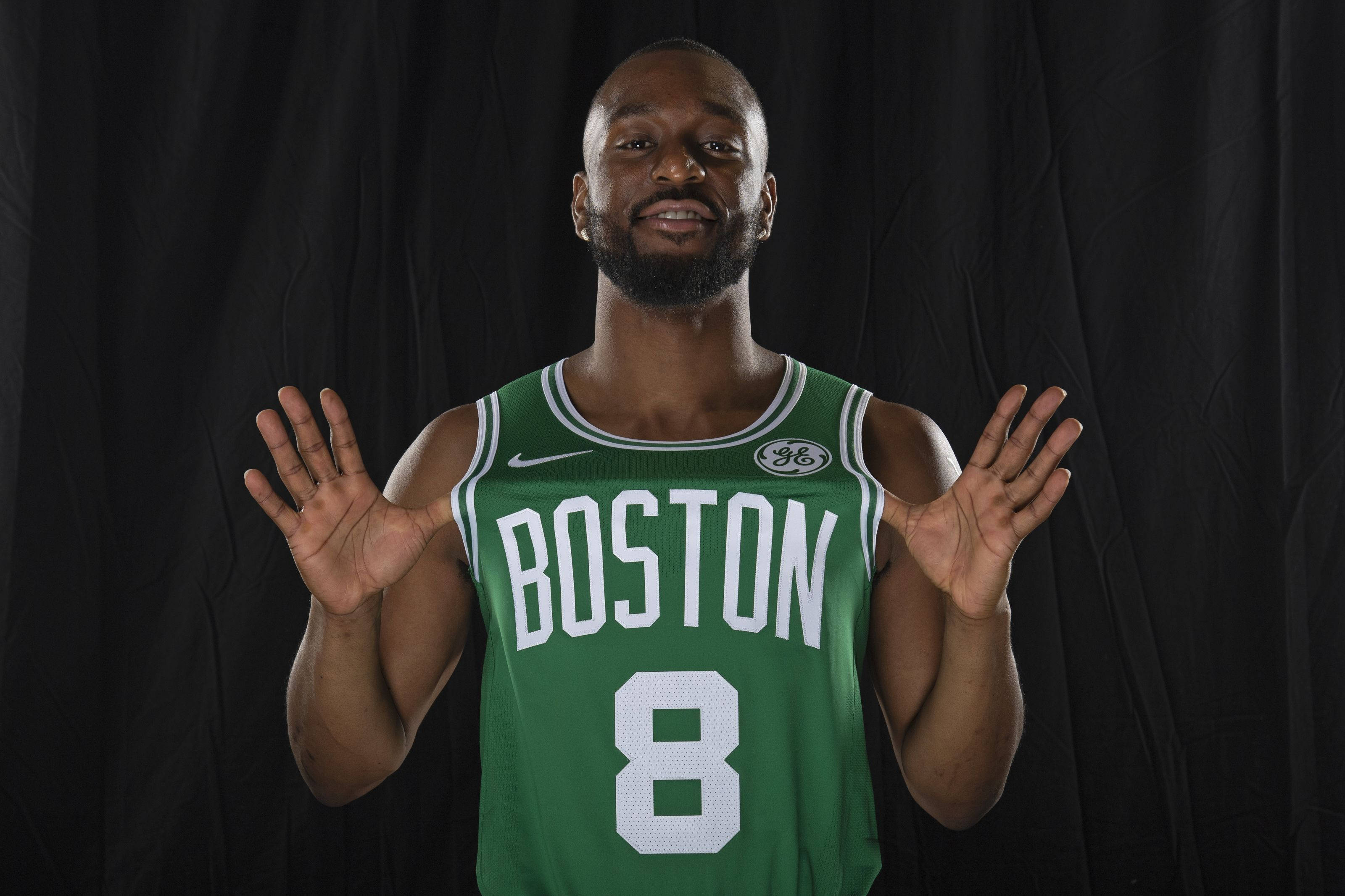 Kemba Walker 桌布 壁紙 — 一名身穿綠色波士頓球衣8號的籃球運動員在黑色背景前張開雙手微笑。