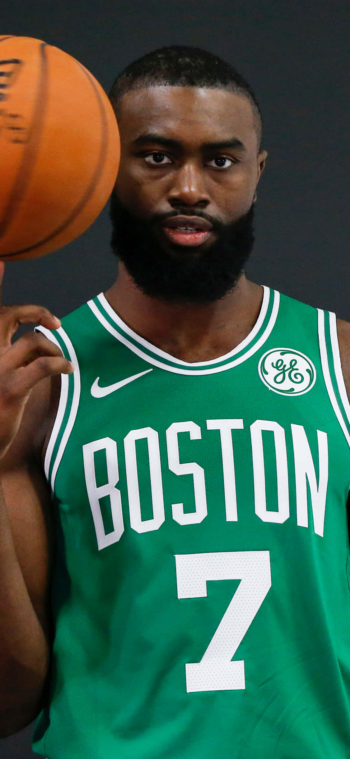 iPhone Xs Basketball 桌布 壁紙 — 一名身穿綠色波士頓球衣的籃球運動員在深色工作室背景下拿著橙色球。