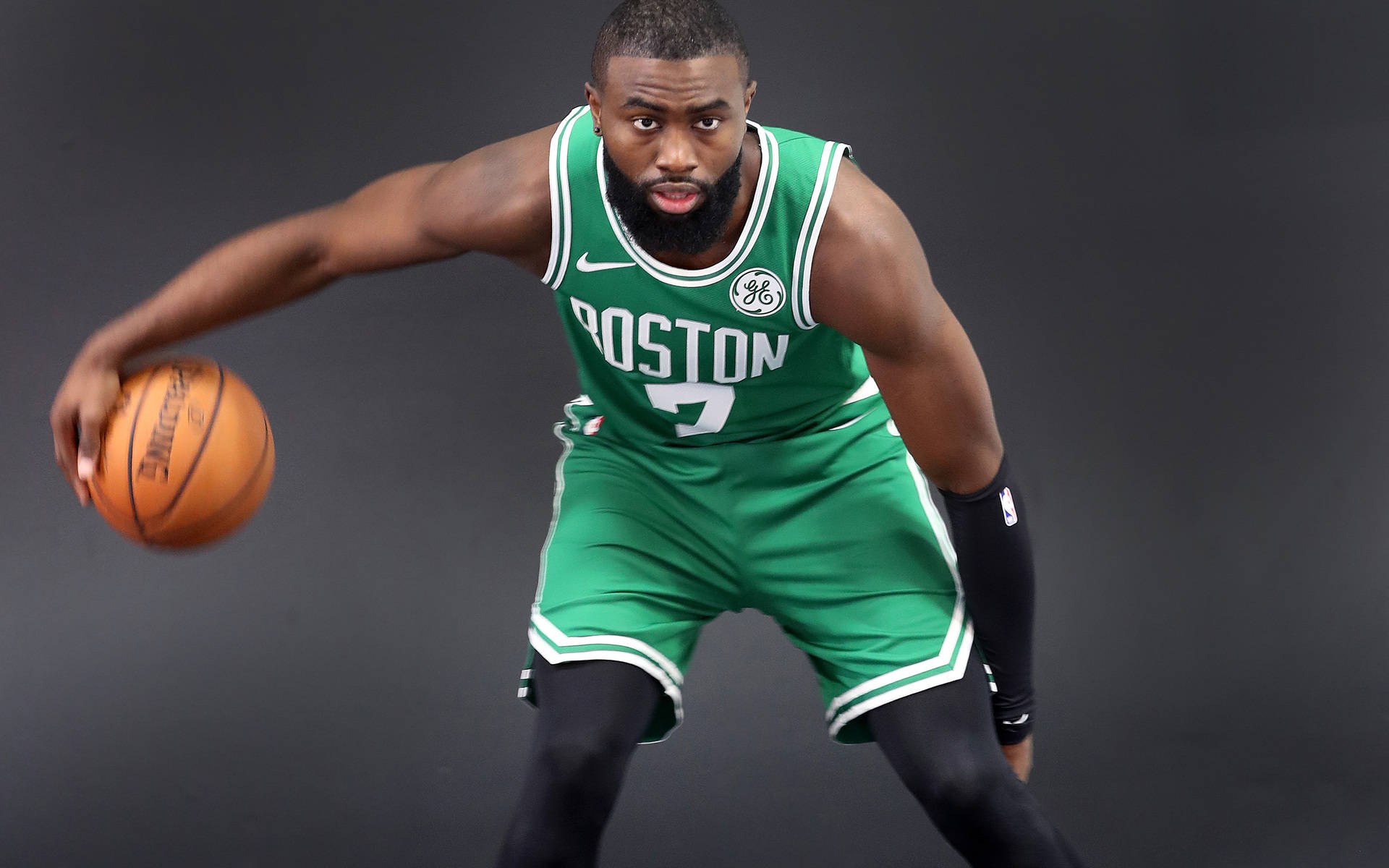 Jaylen Brown 桌布 壁紙 — 一名身穿綠色波士頓球衣的籃球運動員在黑暗的攝影棚背景下，專注地運球。