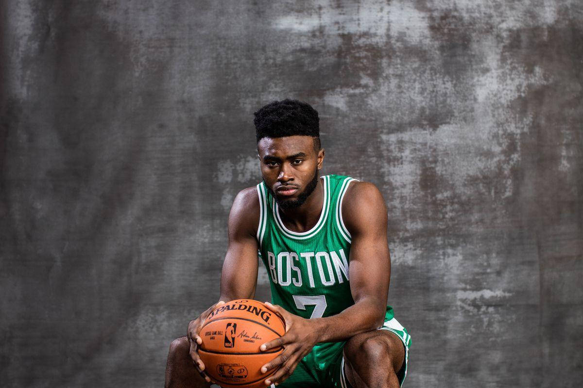 Jaylen Brown 桌布 壁紙 — 一名身穿綠色波士頓球衣的籃球運動員蹲著，手持橙色Spalding籃球，背景為有紋理的灰色。
