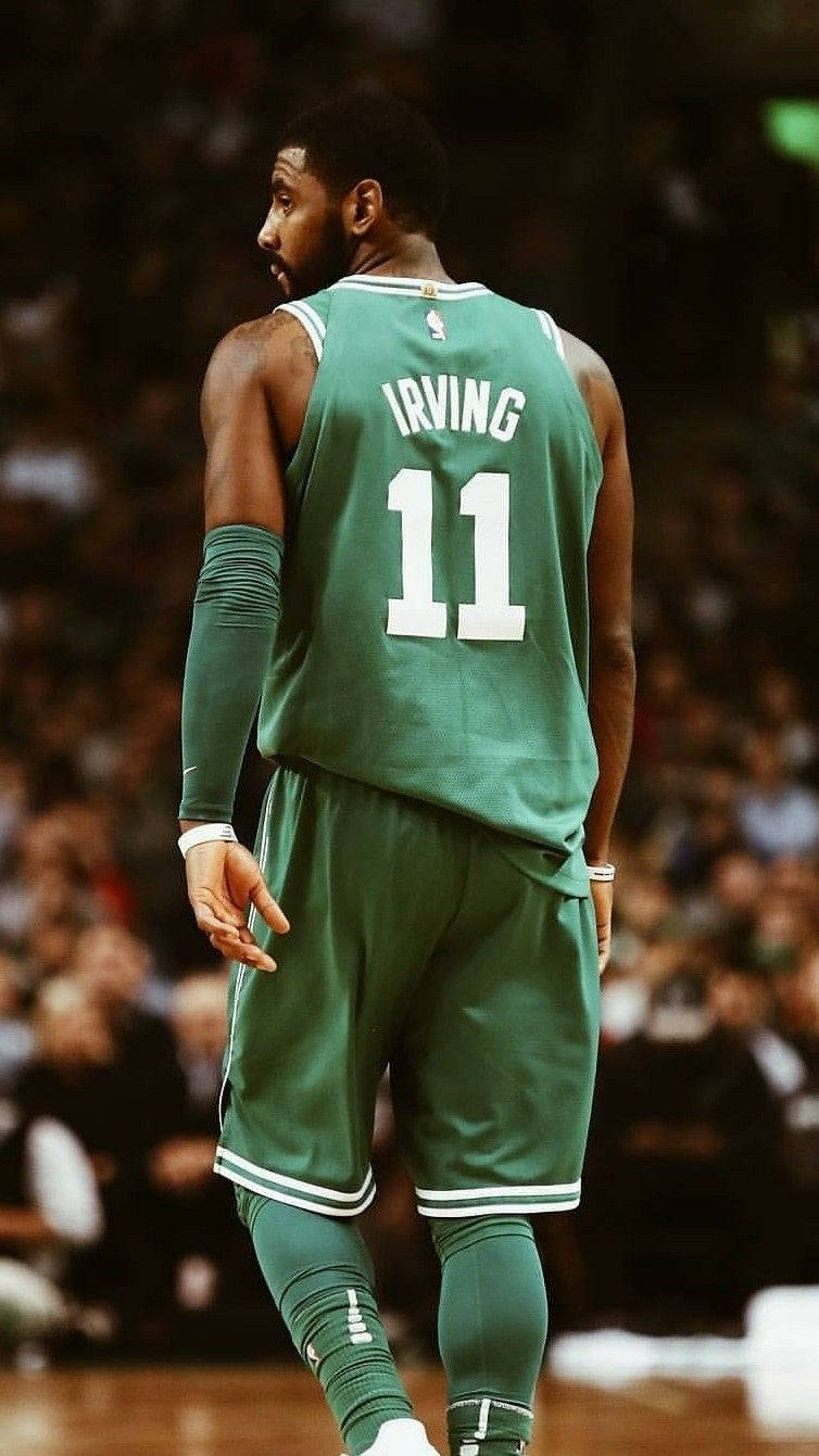 Kyrie 桌布 壁紙 — 一名身穿綠色球衣、印有IRVING名字和11號的籃球運動員站在球場上，背景是模糊的人群。
