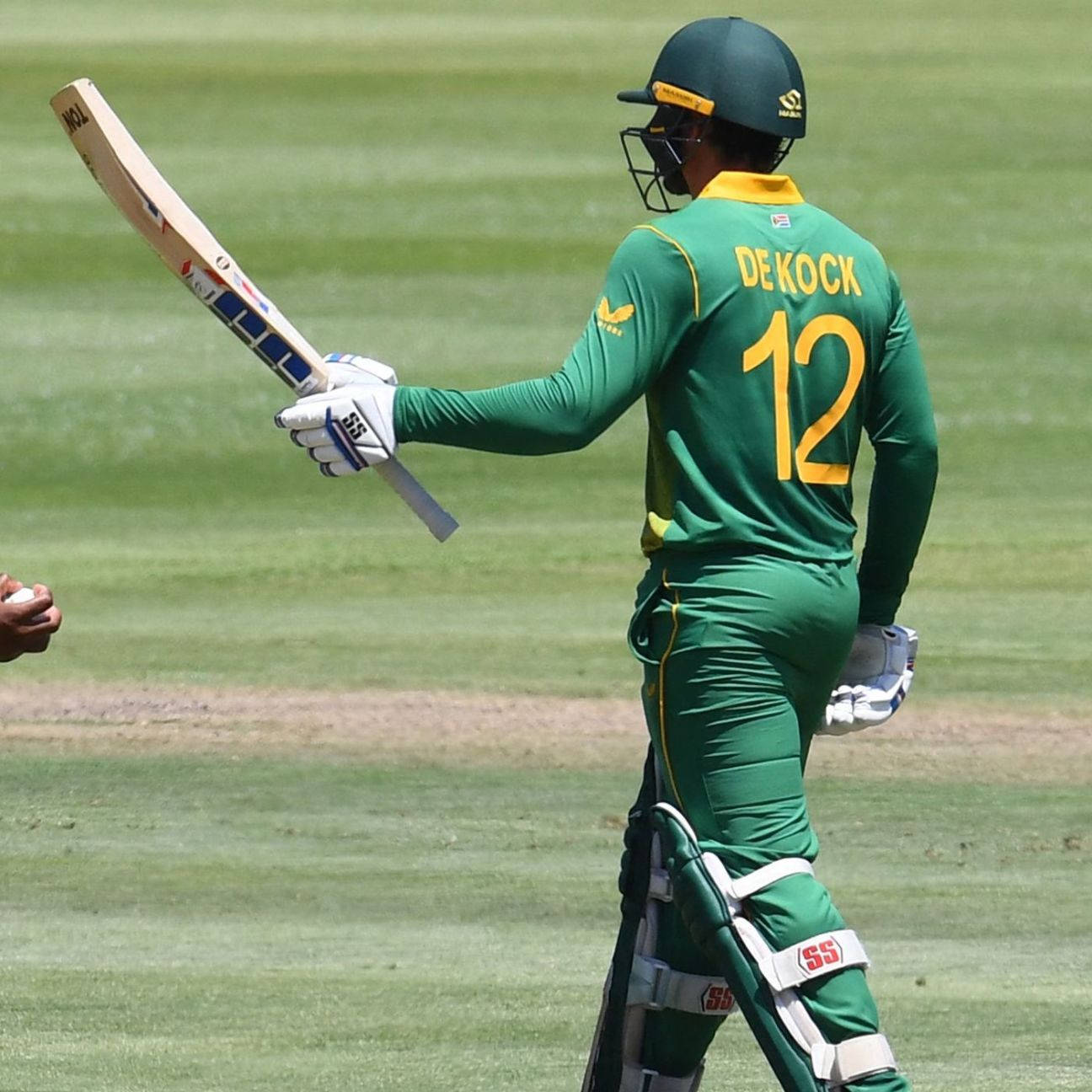 quinton de kock 桌布 壁紙 — 一名身穿綠色球衣、號碼12的板球運動員在明亮的日光下拿著球棒離開球場。