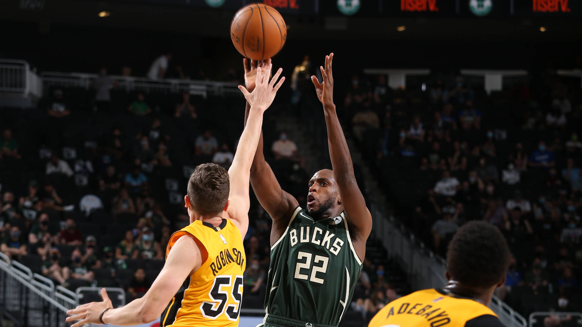 Khris Middleton 桌布 壁紙 — 一名身穿綠色球衣22號的密爾瓦基公鹿球員跳起投籃，而一名身穿黃色球衣的防守球員在擠滿觀眾的場館中跳起封阻他。