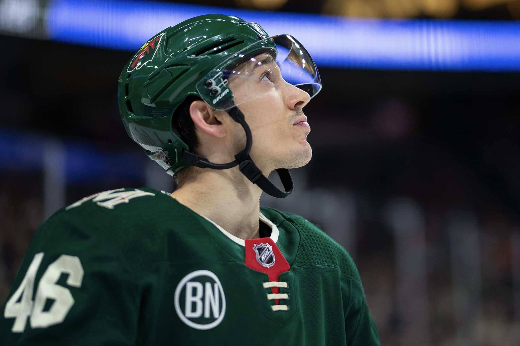 hockey 桌布 壁紙 — 一名身穿綠色球衣和頭盔的冰球運動員在明亮的場館燈光下，專注地向上凝視比賽。