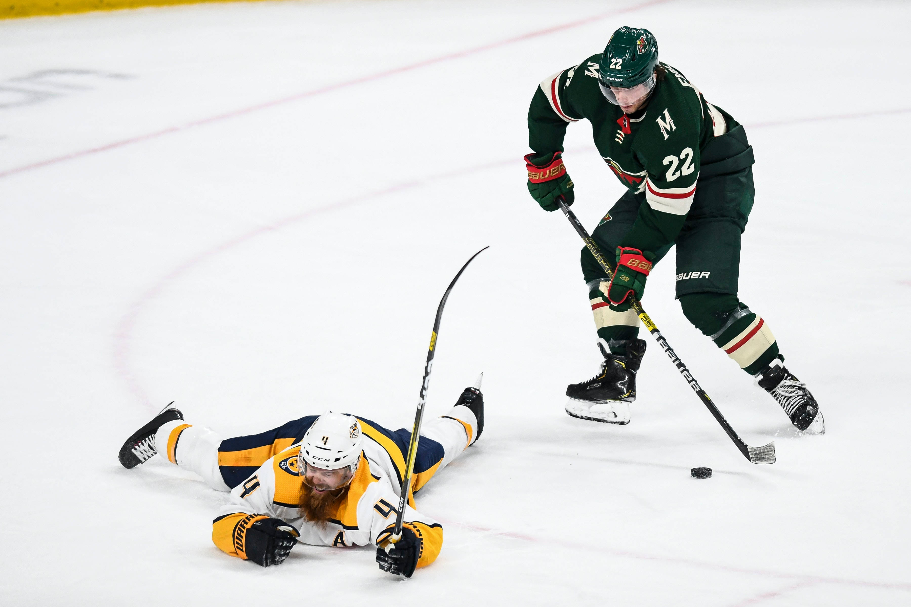 hockey 桌布 壁紙 — 一名身穿綠色球衣的冰上曲棍球運動員向前滑行，而另一名身穿黃色球衣的運動員則倒在冰上靠近冰球的位置。