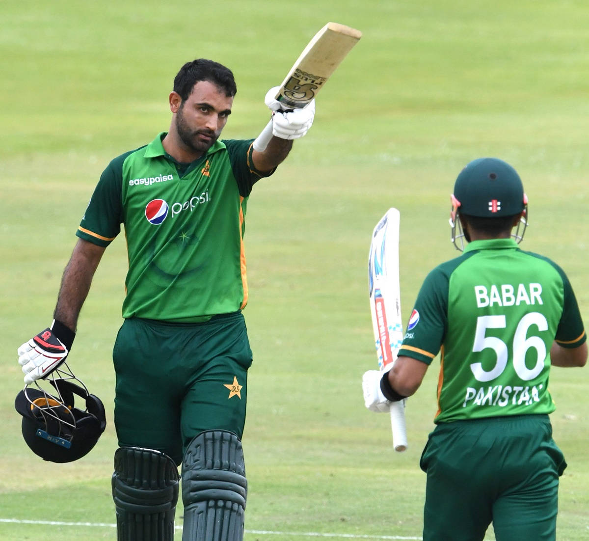 Fakhar Zaman 桌布 壁紙 — 一名身穿綠色球衣的巴基斯坦板球運動員在草地上高舉球棒慶祝勝利，隊友巴巴爾向他致意。