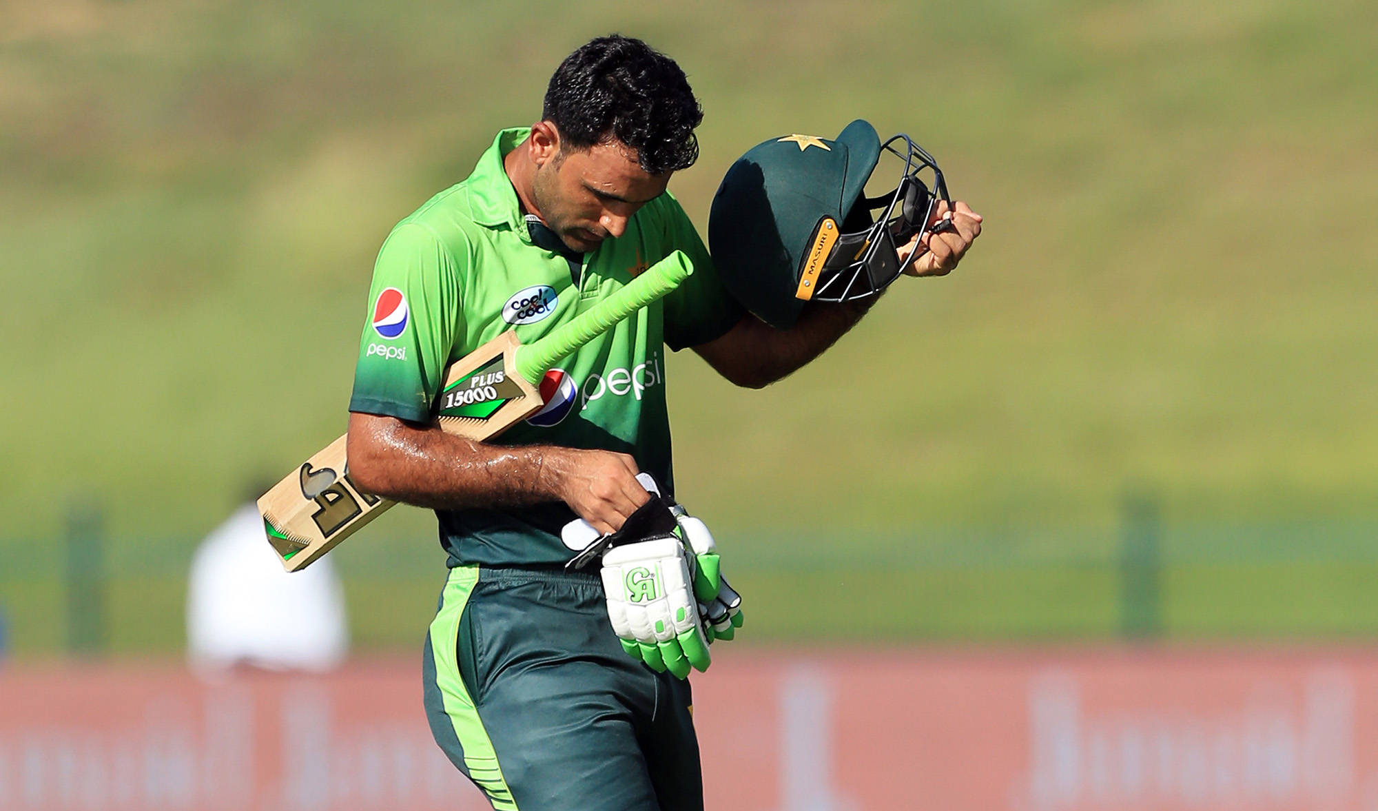 Fakhar Zaman 桌布 壁紙 — 一名身穿綠色球衣的巴基斯坦板球運動員低著頭，手持球棒和頭盔離開球場。