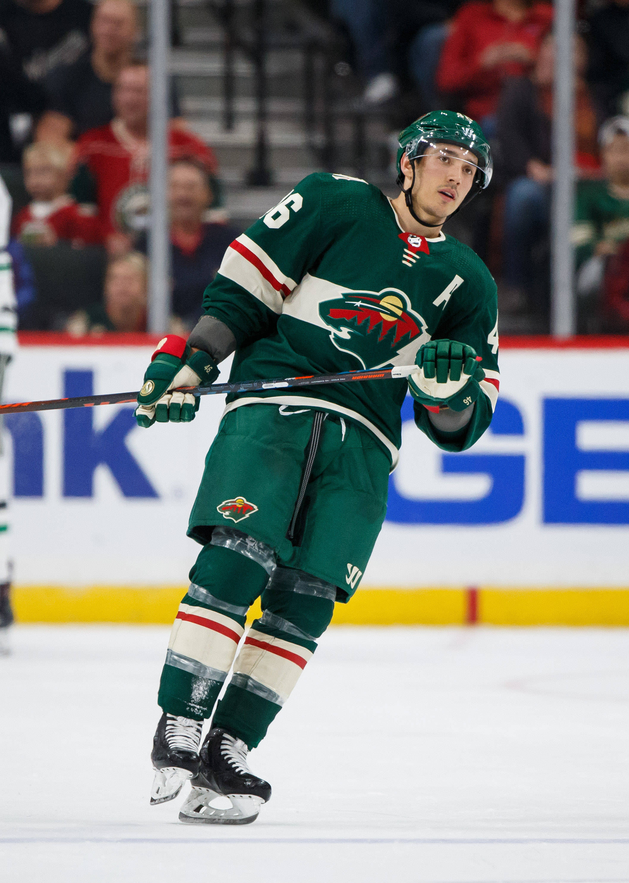 hockey 桌布 壁紙 — 一名身穿綠色球衣的曲棍球運動員在明亮的場館燈光下，在比賽中專注地滑過冰場。