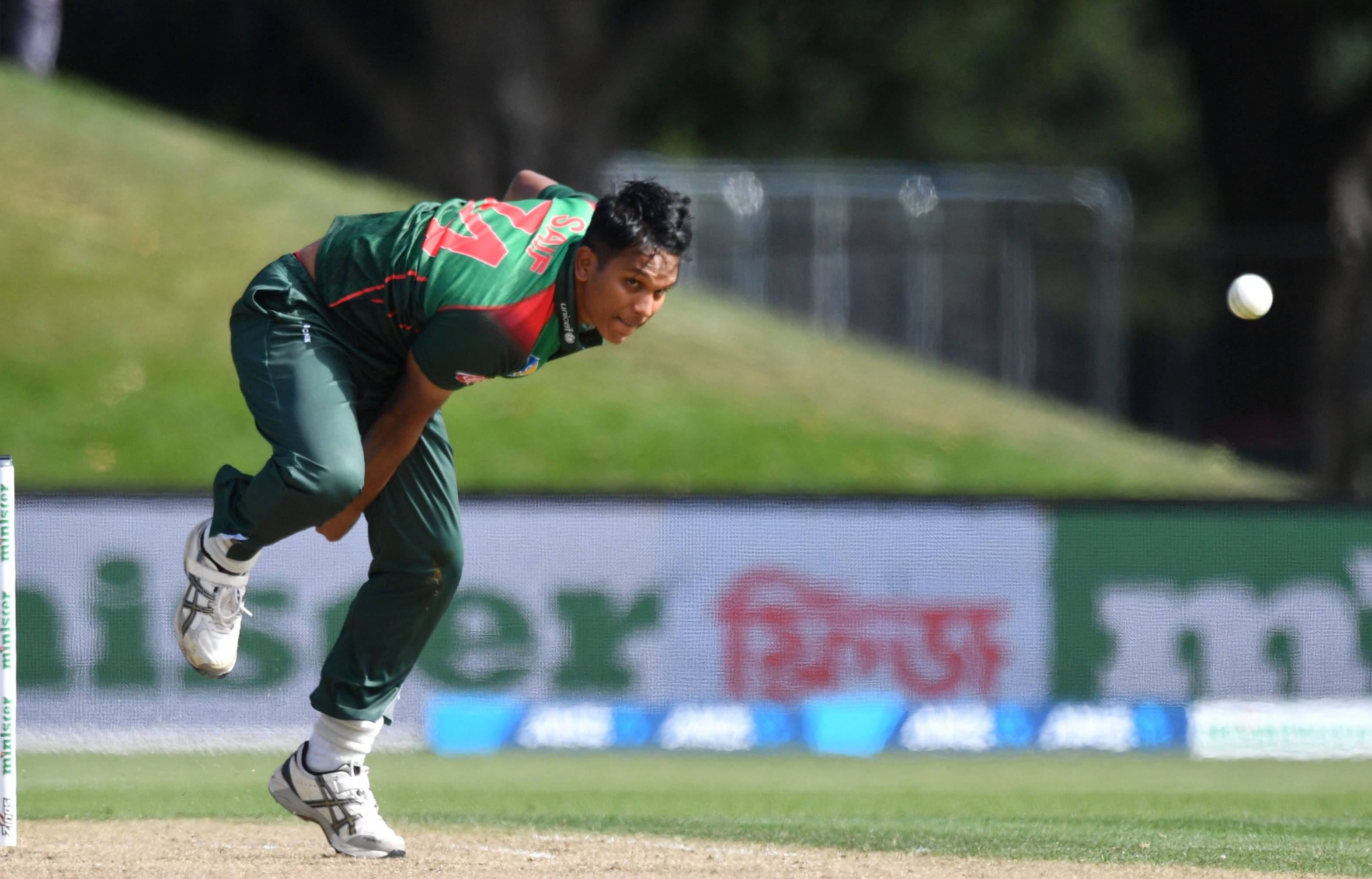 Bangladesh Cricket 桌布 壁紙 — 一名身穿綠色球衣的板球投手在陽光明媚的草地上專注地投球。