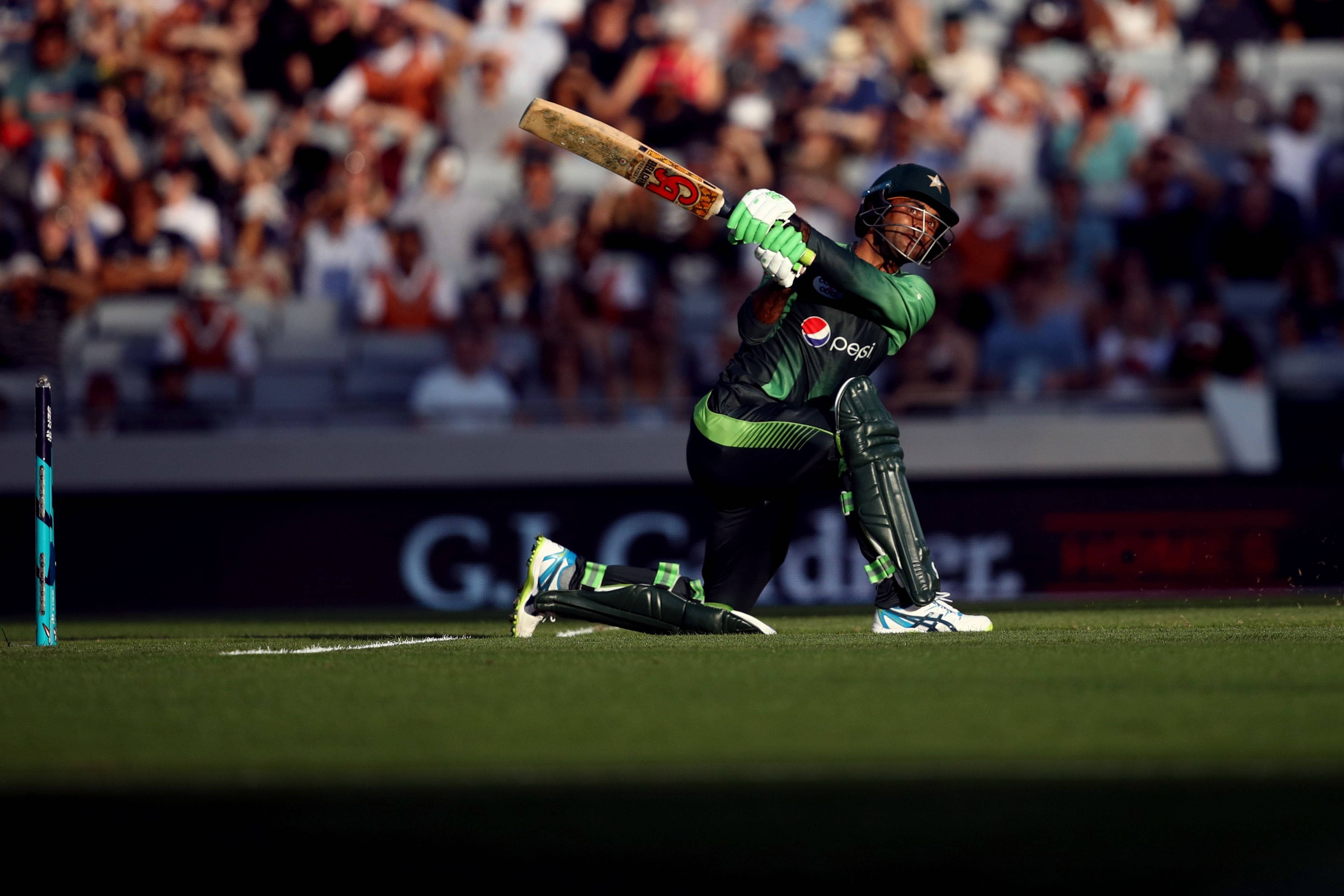 Fakhar Zaman 桌布 壁紙 — 一名身穿綠色球衣的板球運動員在陽光明媚的球場上強力揮棒，背景是模糊的人群。