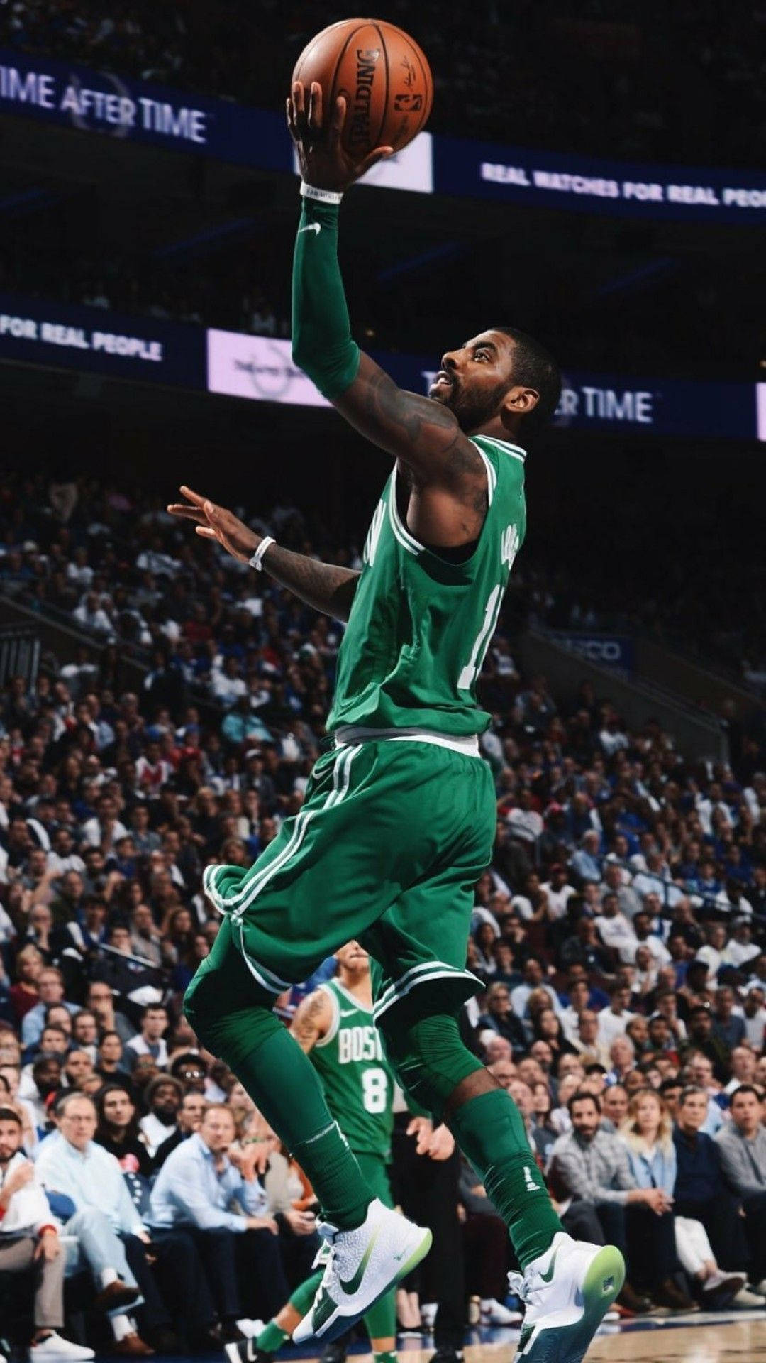 Kyrie 桌布 壁紙 — 一名身穿綠色球衣的籃球運動員在明亮的燈光下，在擠滿觀眾的場館中高高躍起投籃。