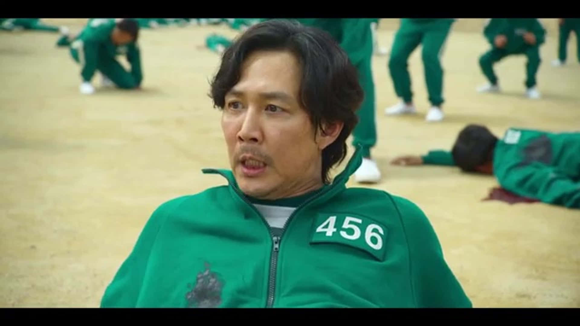 Characters 桌布 壁紙 — 一名身穿綠色號碼運動服的男子看起來很震驚，而其他人則一動不動地躺在塵土飛揚的場地上。