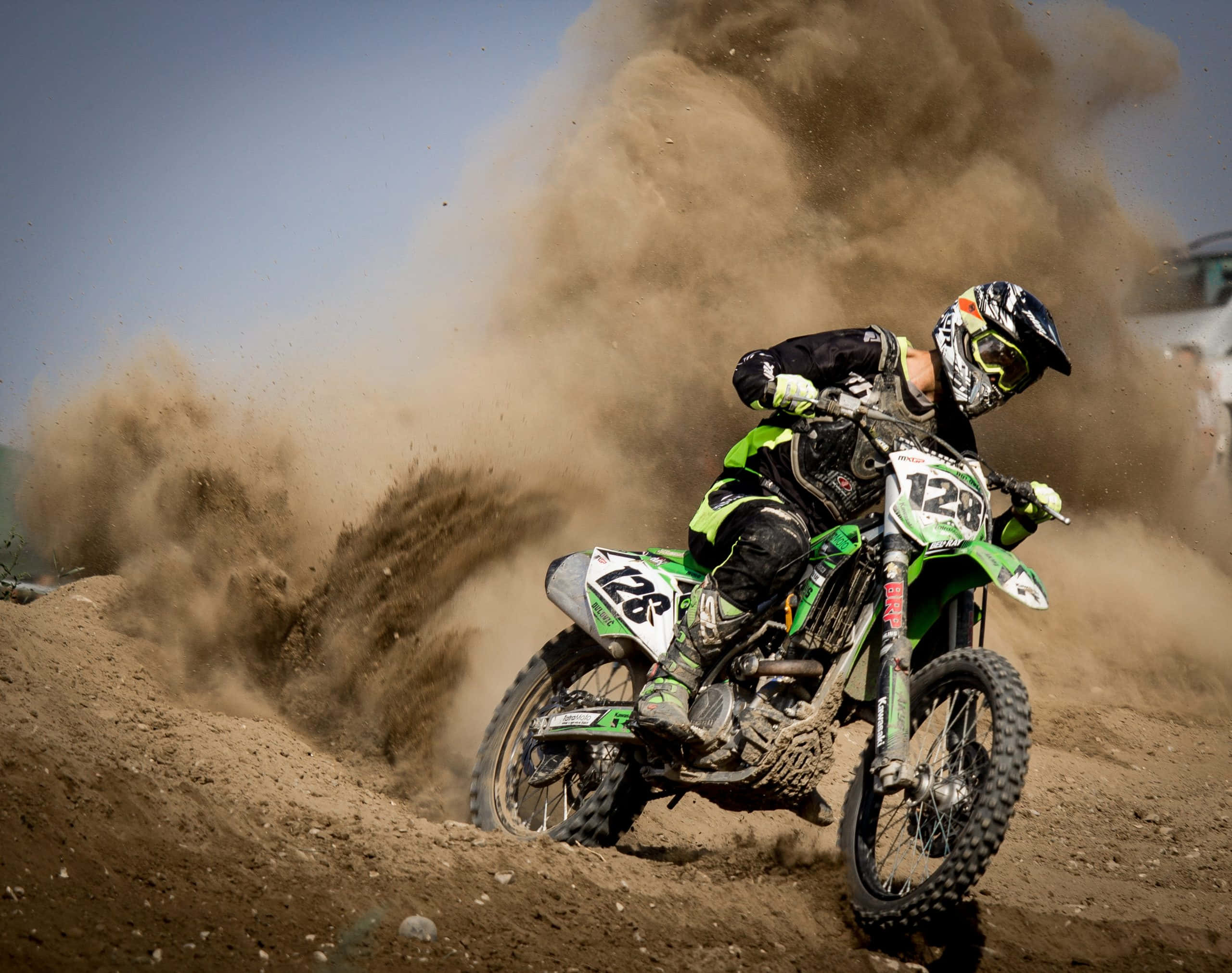 Dirtbike 桌布 壁紙 — 一名身穿綠色裝備的越野摩托車手在泥地賽道上傾斜入彎，揚起大片棕色塵土。