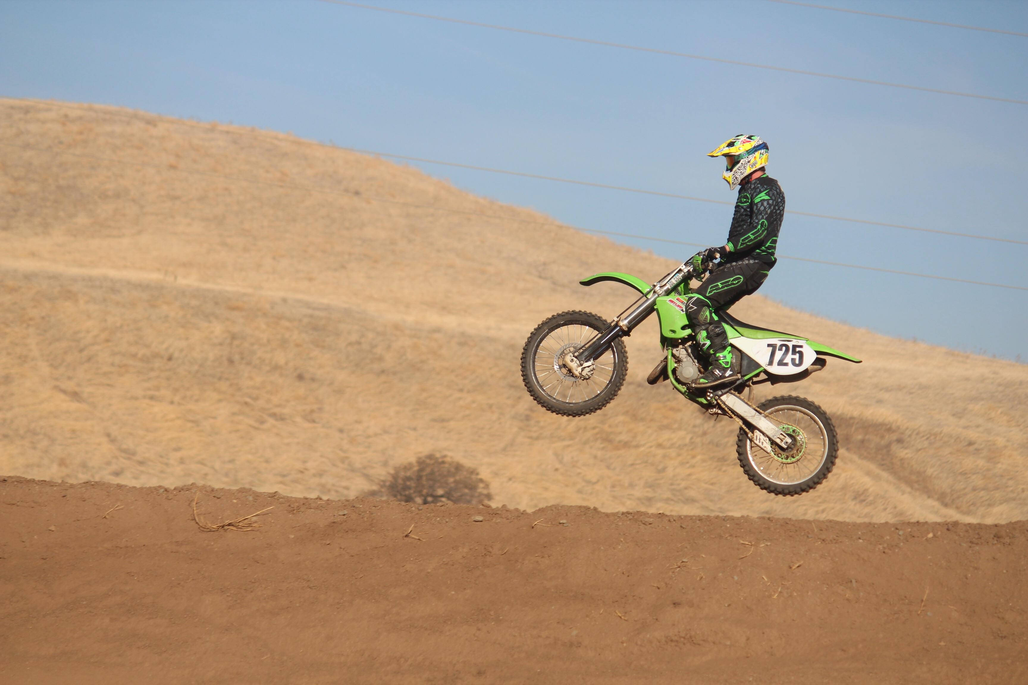 Ronnie Mac 桌布 壁紙 — 一名身穿綠色裝備的越野機車手在晴朗藍天下，騎著泥地機車飛越沙丘。