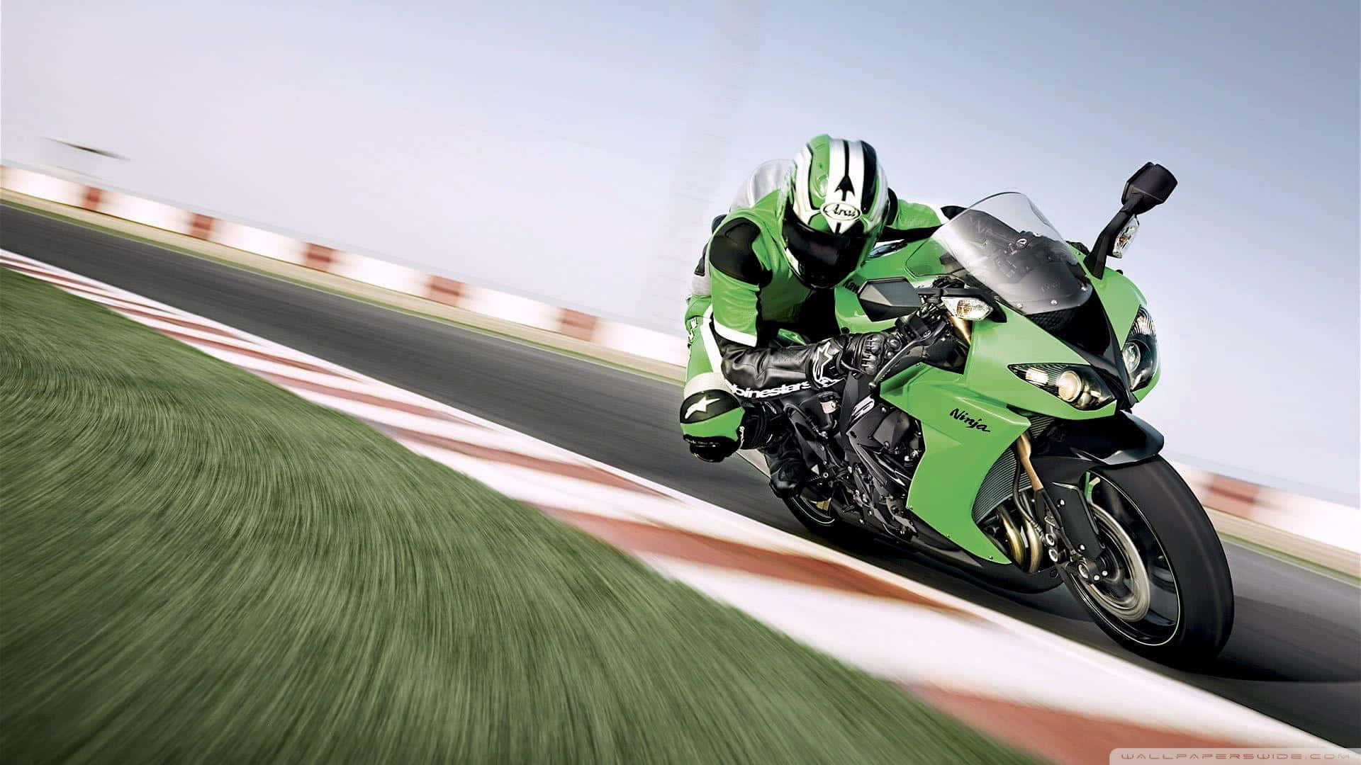 Kawasaki Desktop 桌布 壁紙 — 一名身穿綠色裝備的騎士在賽道上騎著鮮綠色的川崎忍者摩托車，傾斜入彎，背景有模糊的草地和紅白路緣。