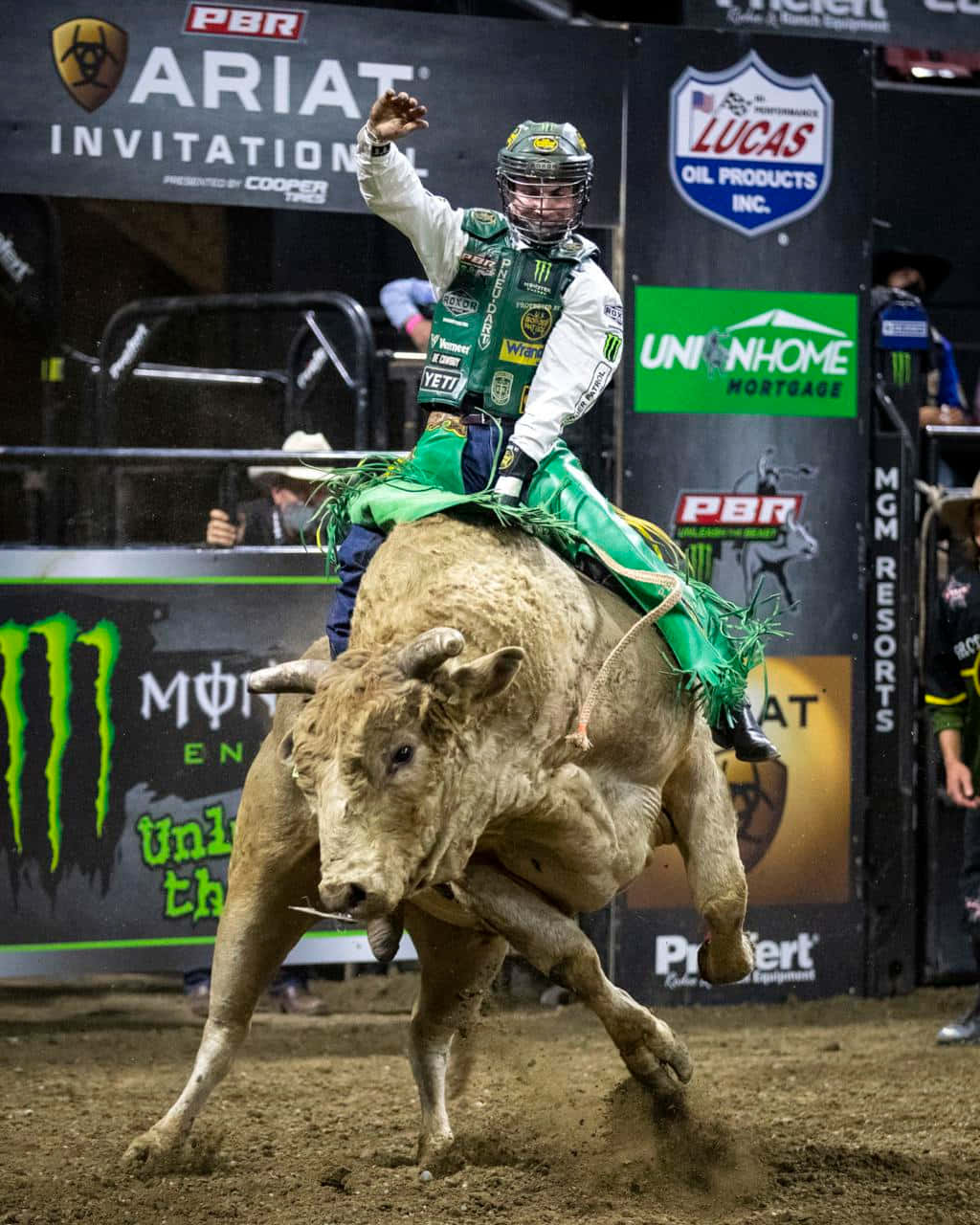 Bull Riding 桌布 壁紙 — 一名身穿綠色裝備的鬥牛騎士在競技場燈光下，背景有贊助商橫幅，緊緊抓住一頭狂跳的牛。