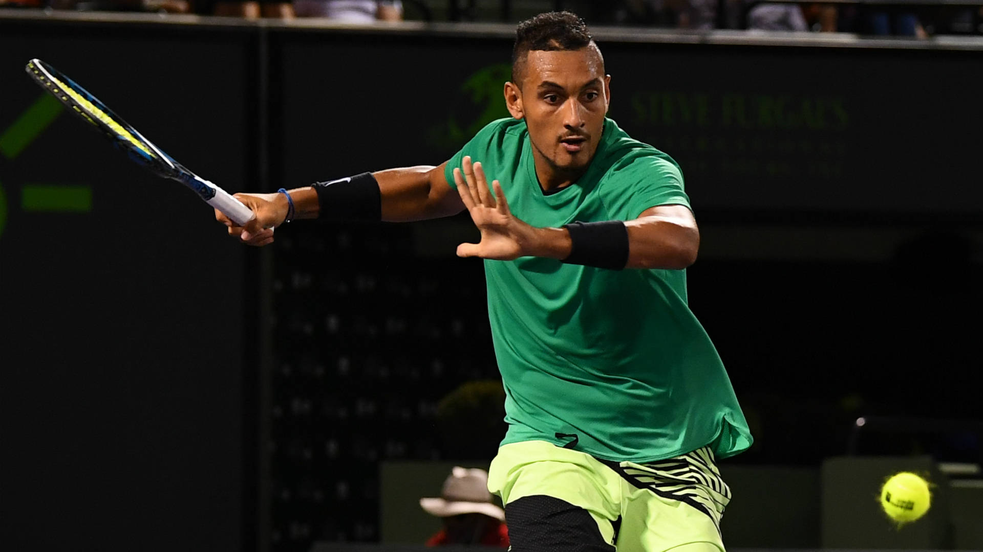 Kyrgios 桌布 壁紙 — 一名身穿綠色襯衫和螢光短褲的男網球選手在明亮燈光下進行激烈比賽時揮拍擊打黃色球。