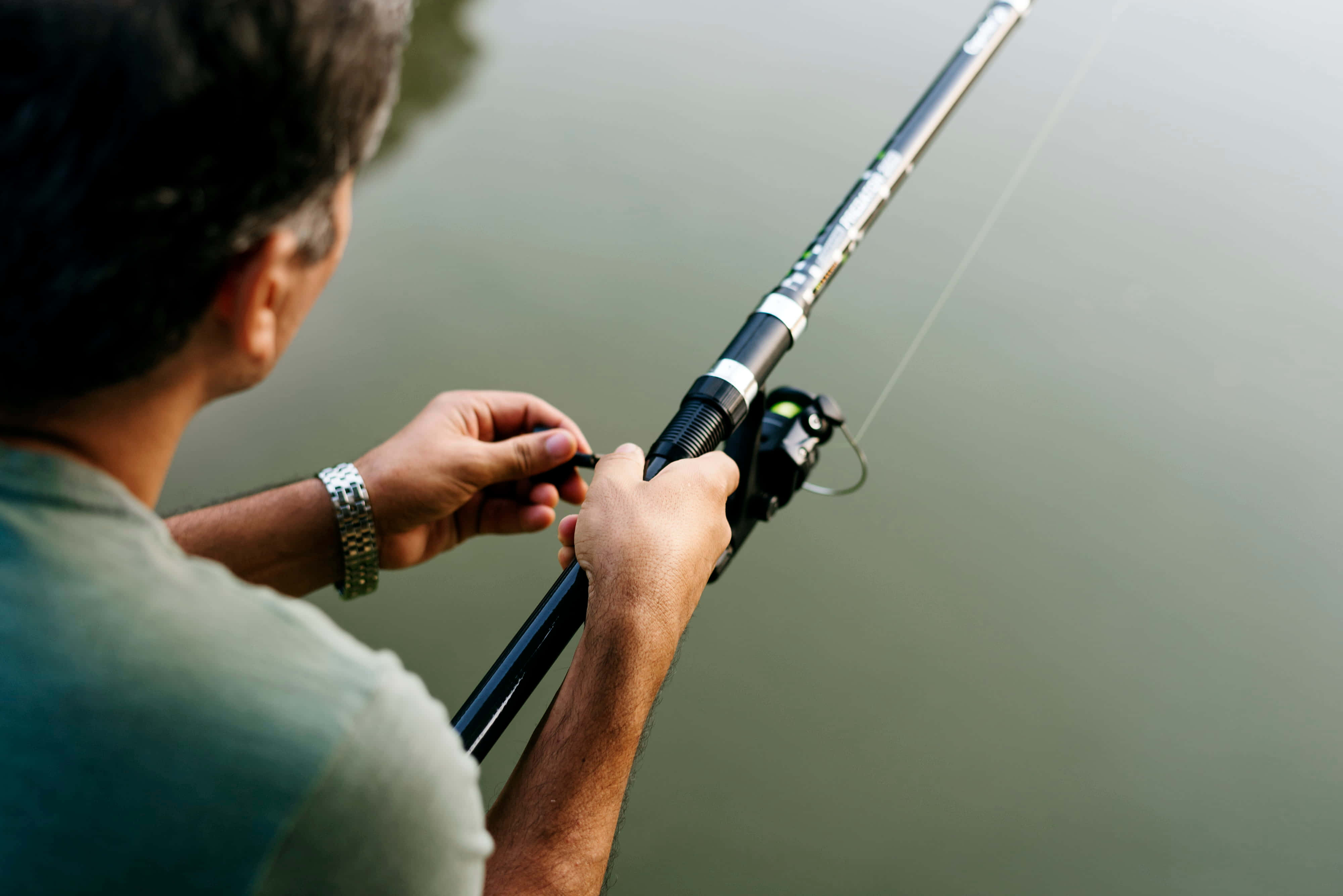 Fishing Bait 桌布 壁紙 — 一名身穿綠色襯衫的男子在寧靜的湖邊將釣竿拋入平靜的水中。