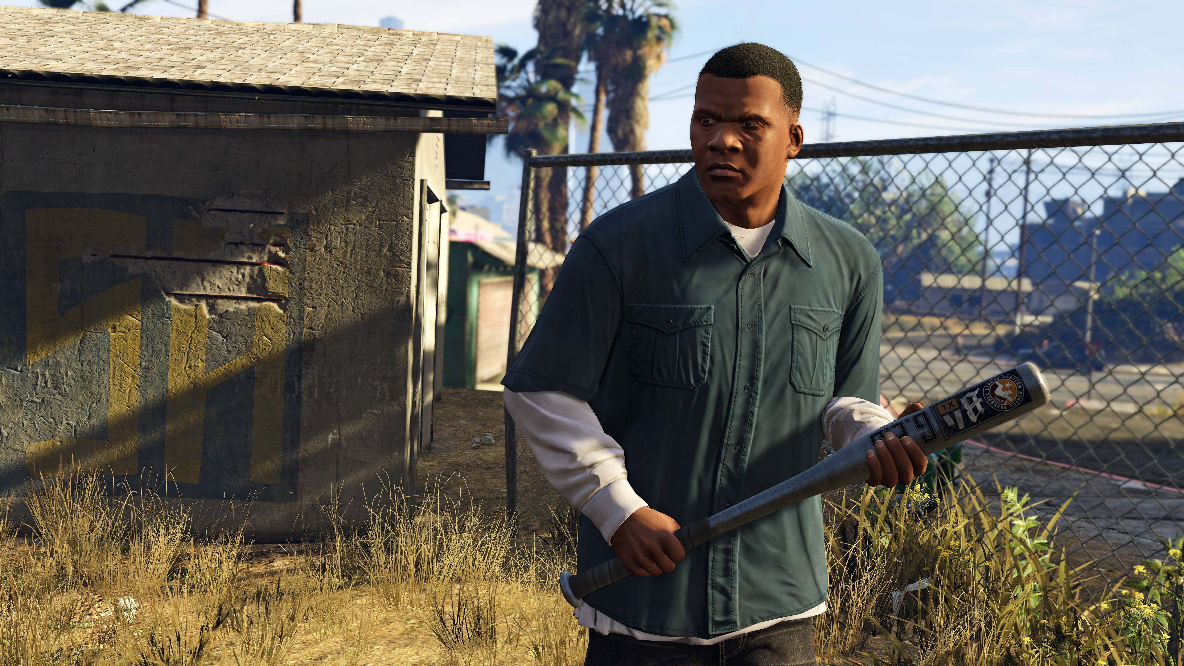 Gta 桌布 壁紙 — 一名身穿綠色襯衫的男子在陽光明媚的城市小巷中手持棒球棒，周圍有鐵絲網圍欄和棕櫚樹。