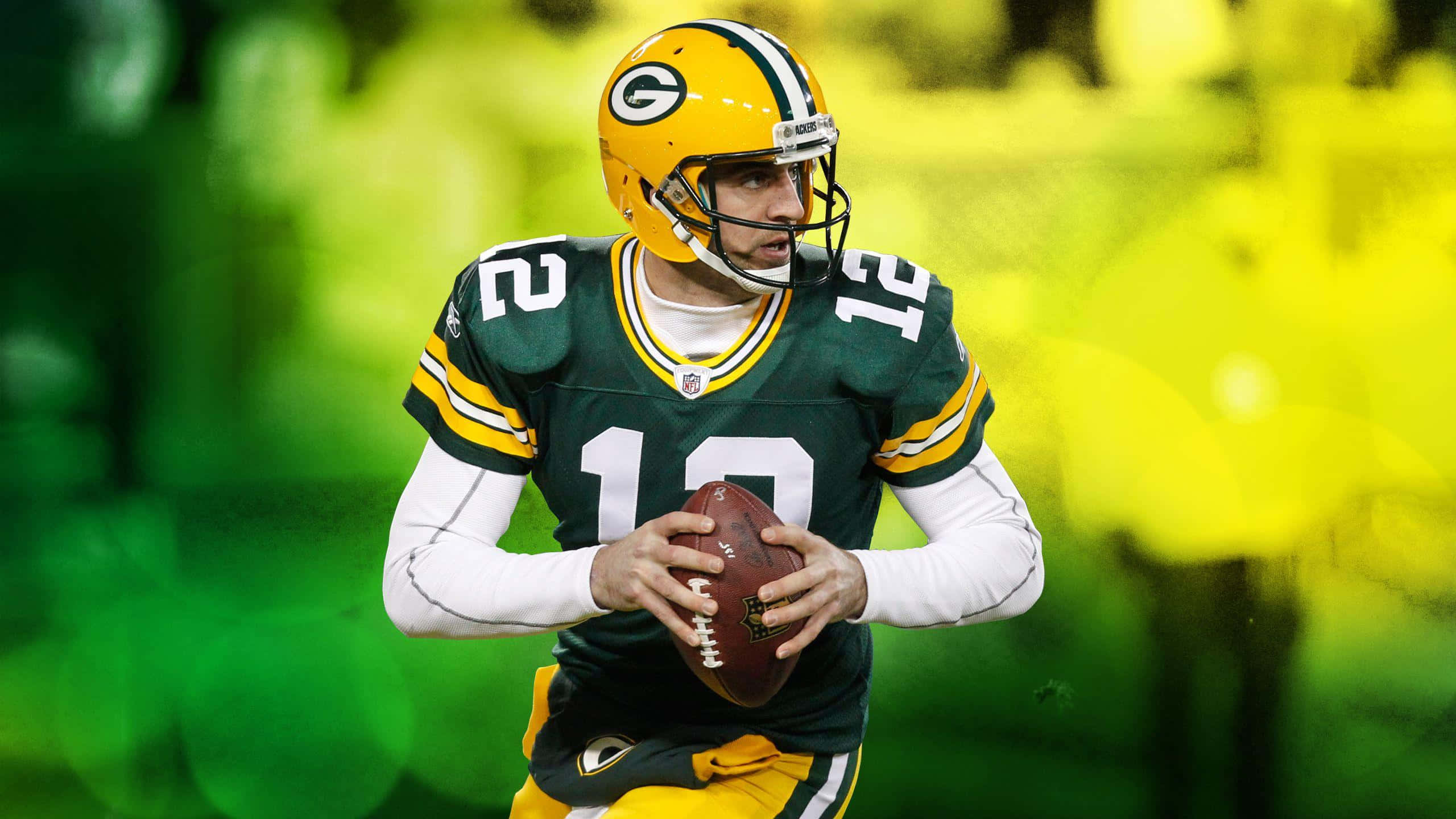 Aaron Rodgers 桌布 壁紙 — 一名身穿綠金球衣的綠灣包裝工四分衛在模糊的球場背景下持球進行比賽。
