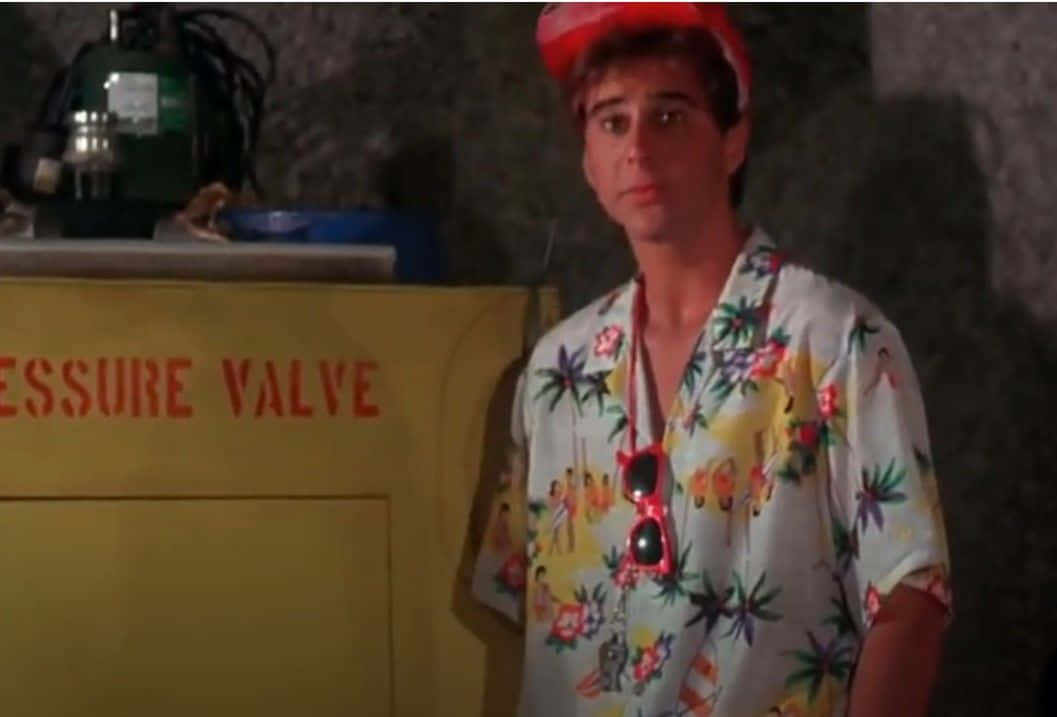 Jonathan Silverman 桌布 壁紙 — 一名身穿色彩繽紛熱帶襯衫和紅色帽子的男子，站在昏暗工業環境中的黃色壓力閥櫃旁。