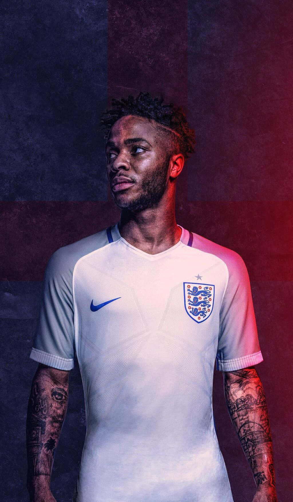 Sterling 桌布 壁紙 — 一名身穿英格蘭白色球衣的足球員站在紅色和深藍色紋理背景前，手臂上的刺青清晰可見。