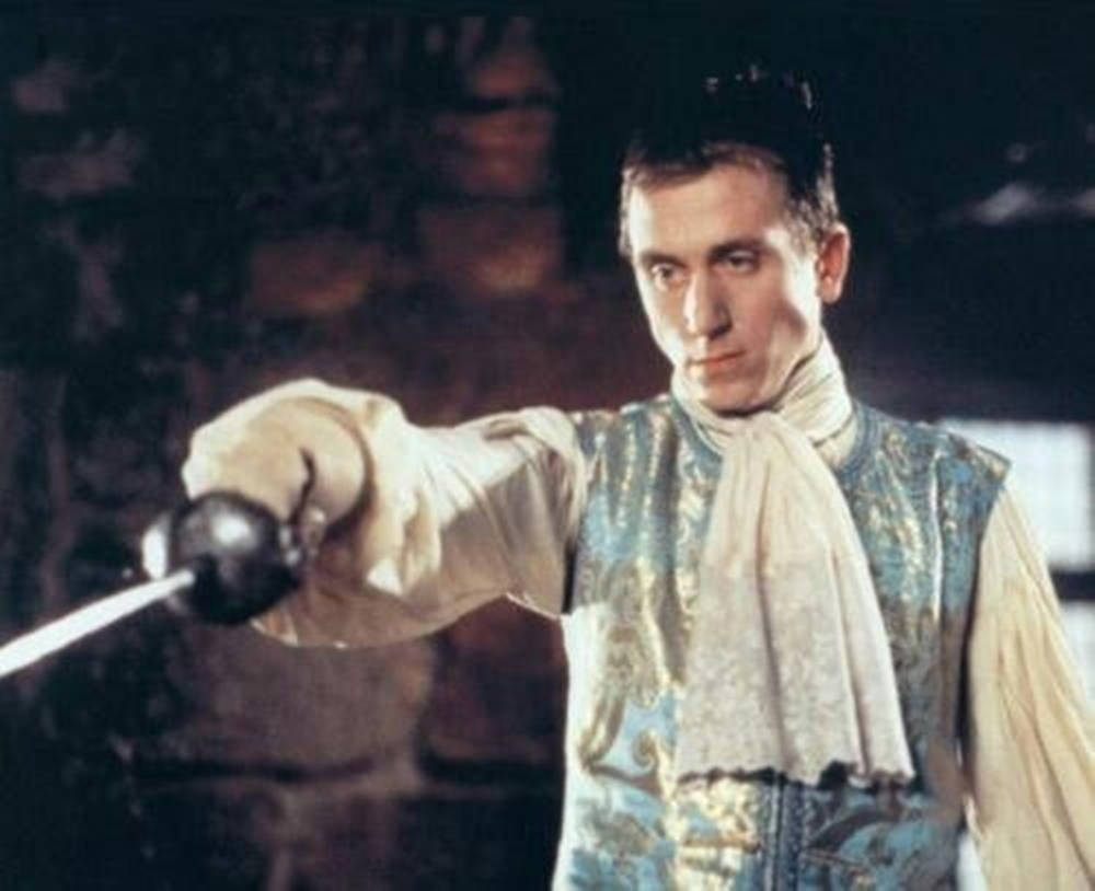 Medieval 桌布 壁紙 — 一名身穿華麗藍金色歷史服裝的男子，在光線昏暗的石室中，專注地將劍向前伸出。
