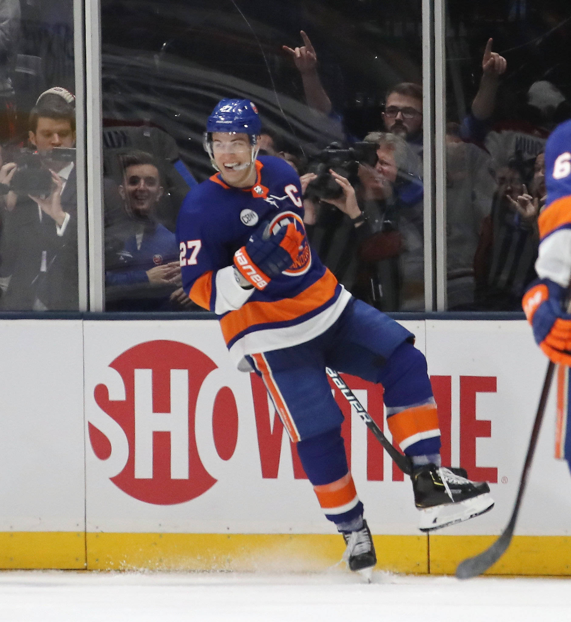 New York Islanders 桌布 壁紙 — 一名身穿藍橙色球衣的冰球運動員在冰上慶祝進球，玻璃後面的球迷歡呼雀躍。