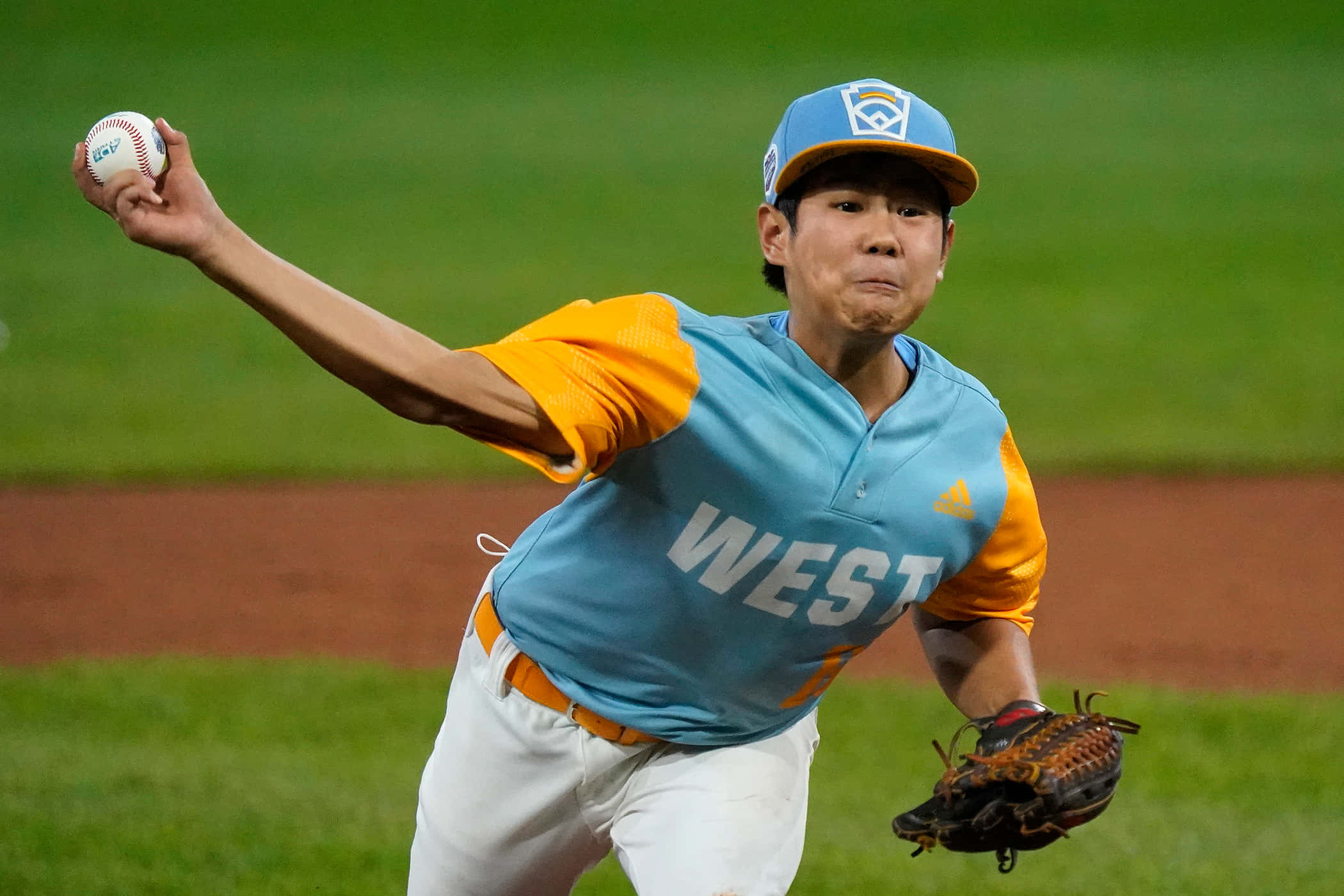 Little League Baseball 桌布 壁紙 — 一名身穿藍橙色球衣的棒球投手在夜間燈光明亮的球場上準備投球。